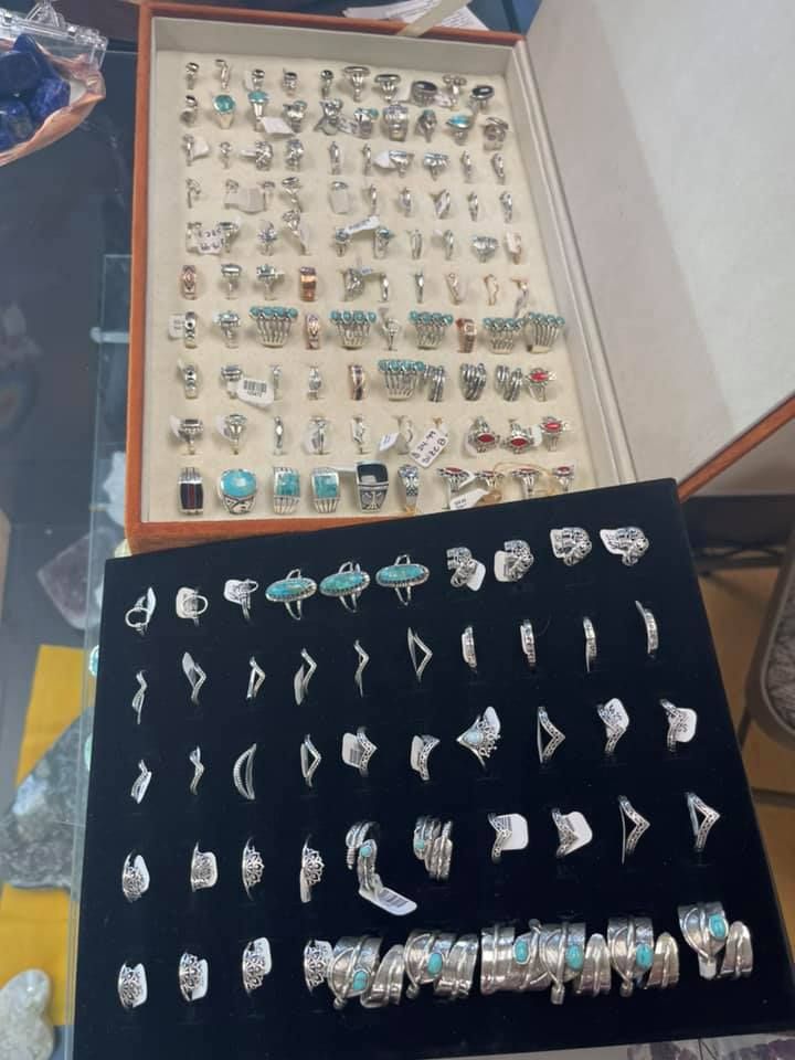 Jewelry display case with rows of silver rings, some with turquoise, on a black and beige surface.