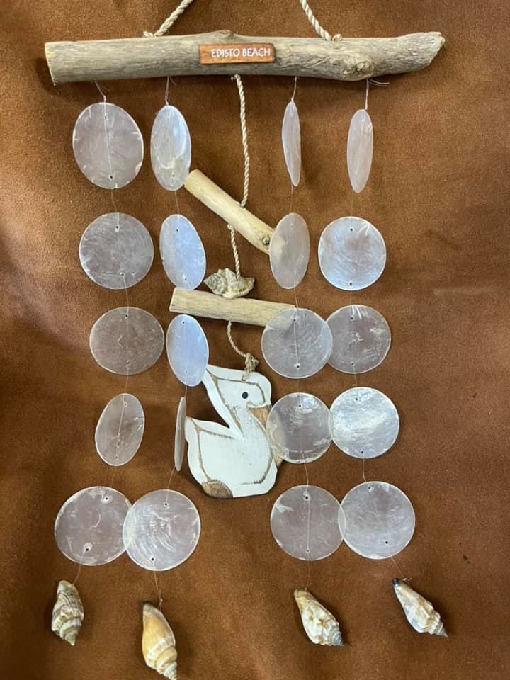 A handcrafted wind chime made of driftwood, shells, and a wooden pelican against a brown background.