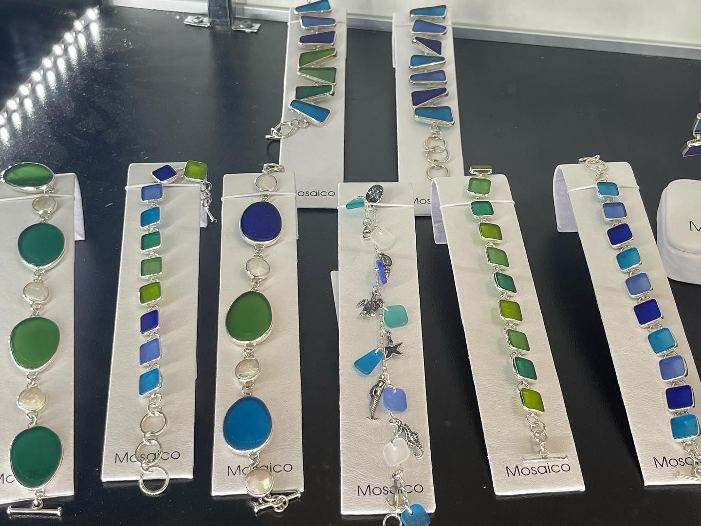 Sea glass bracelets in various blues and greens, displayed on white stands.