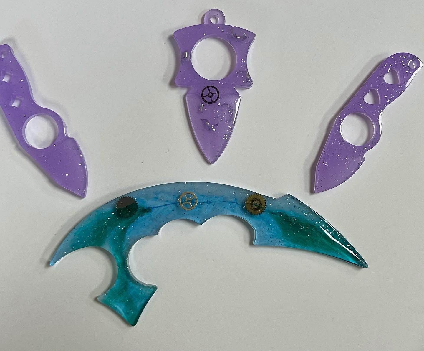 Resin knife charms in various purple and teal hues with glitter and small metal accents.