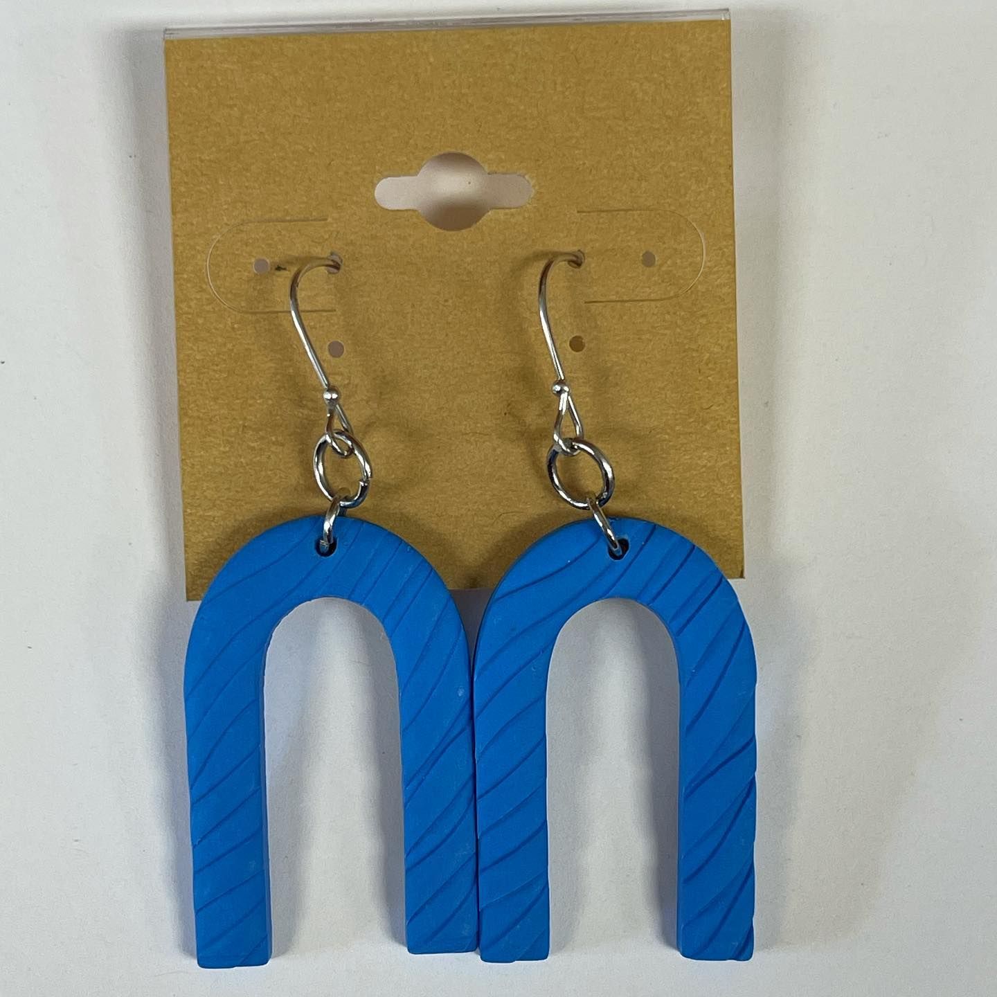 Blue, arch-shaped earrings with silver hooks displayed on a brown card.