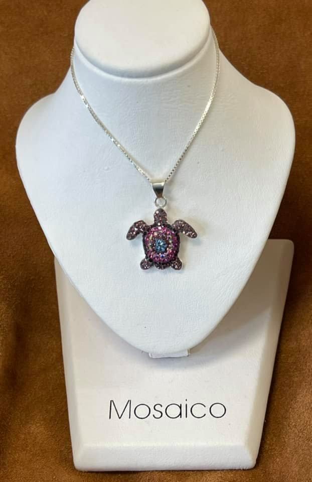 Silver turtle pendant with pink and blue gems on a white jewelry display.
