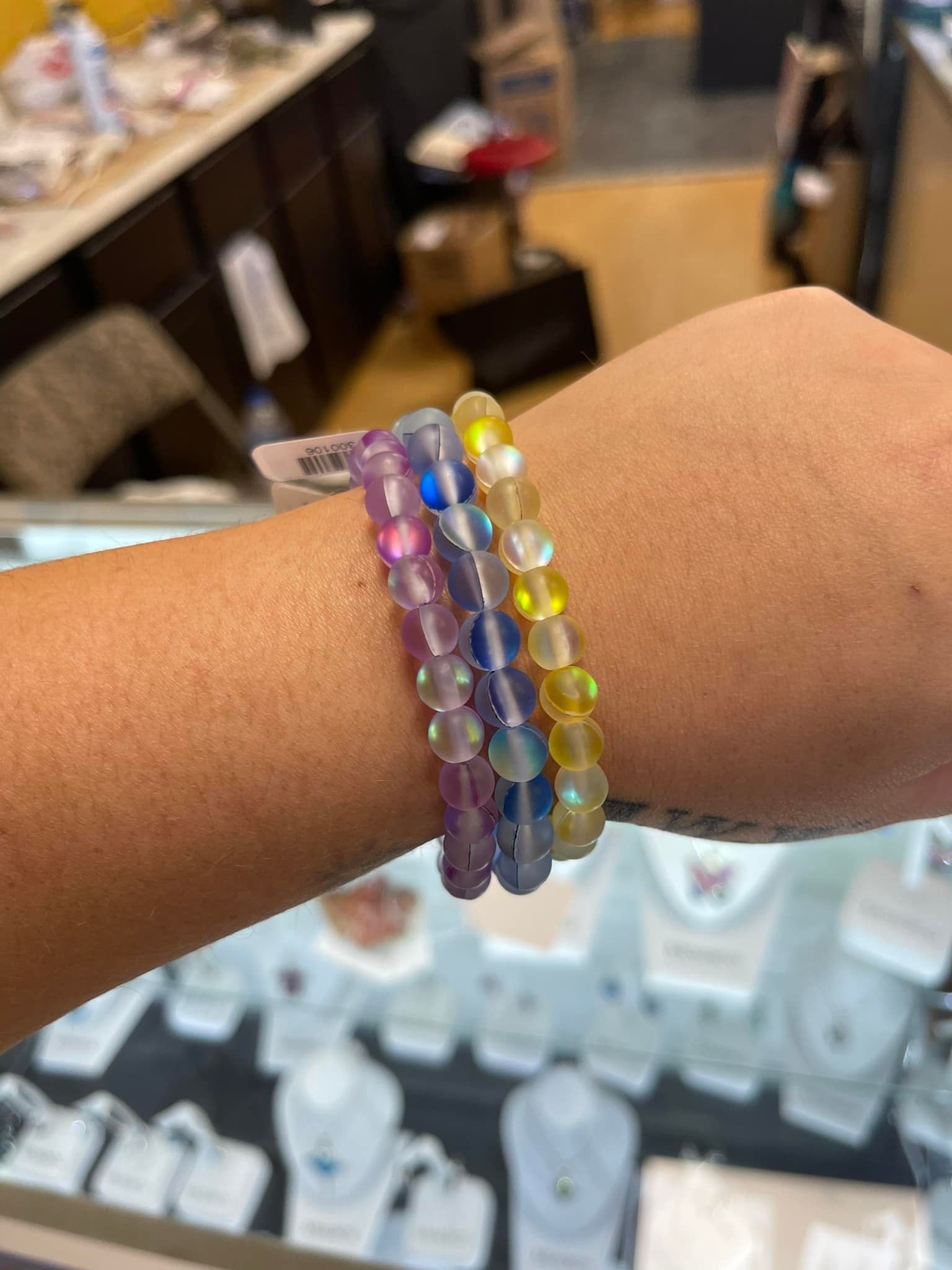 Three iridescent beaded bracelets stacked on a wrist, in purple, blue, and yellow.