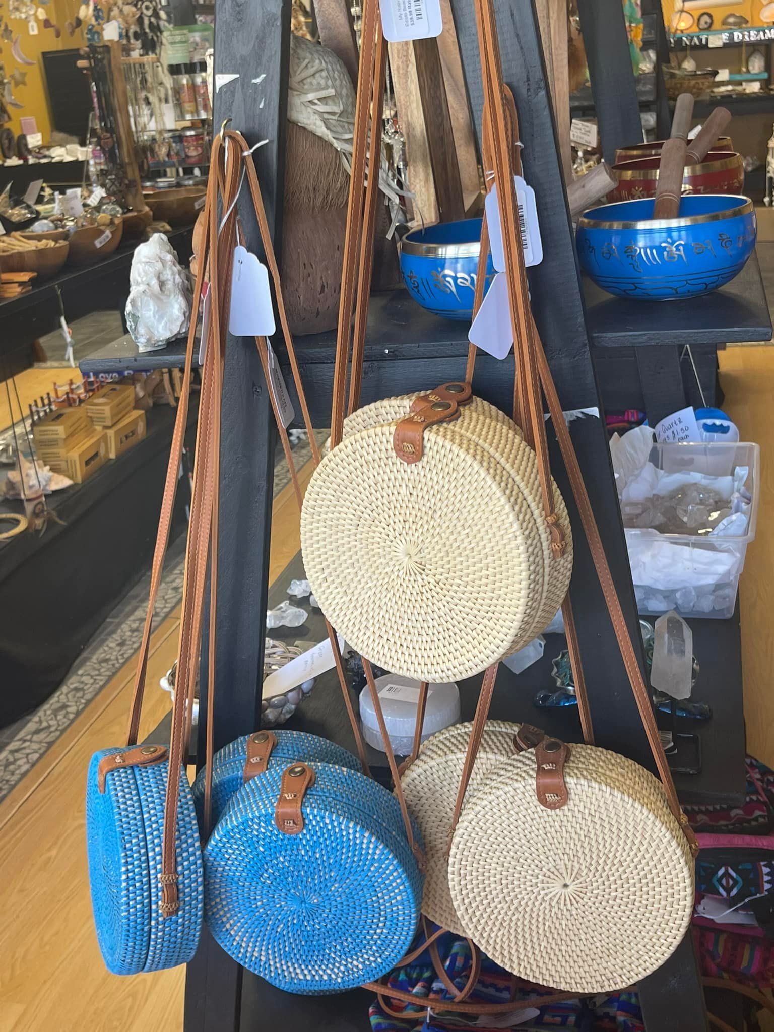 Bags hanging on a display. Woven bags, blue and tan, with brown leather straps and tags.