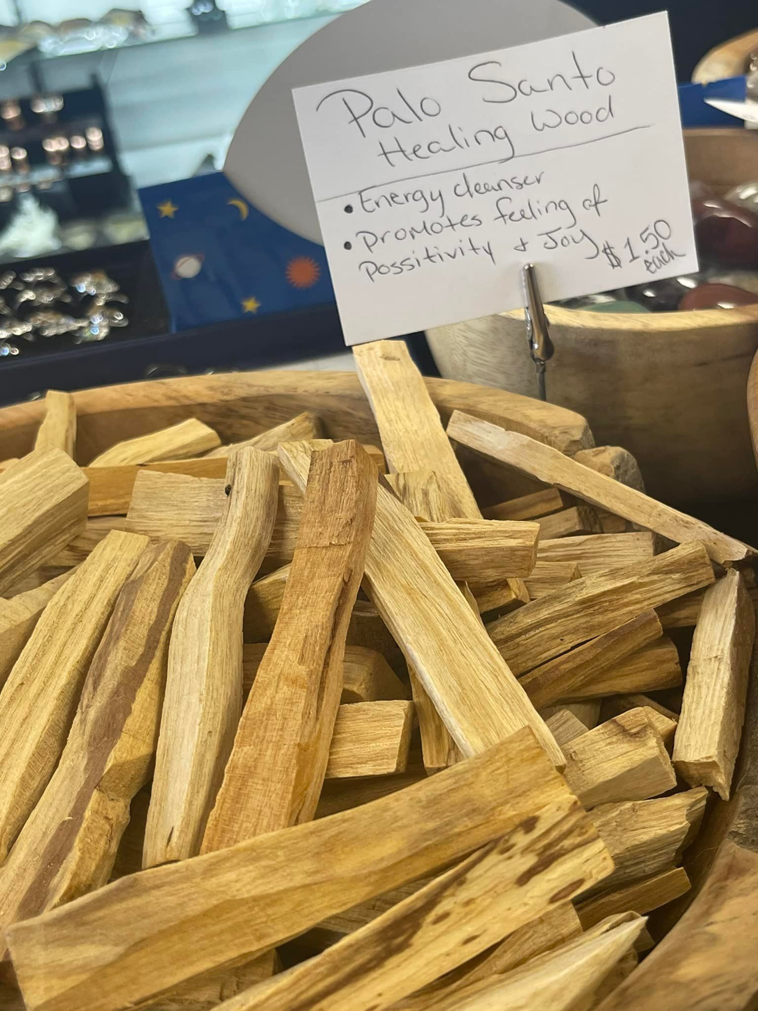 Pile of Palo Santo wood sticks, pale yellow-brown color, in a wooden bowl with a handwritten sign.