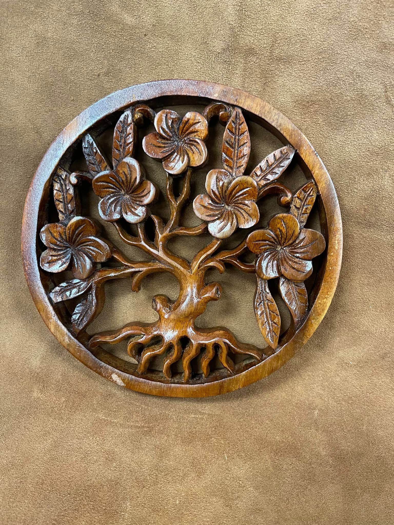 Carved wooden tree of life design with flowers inside a circular frame on a brown background.