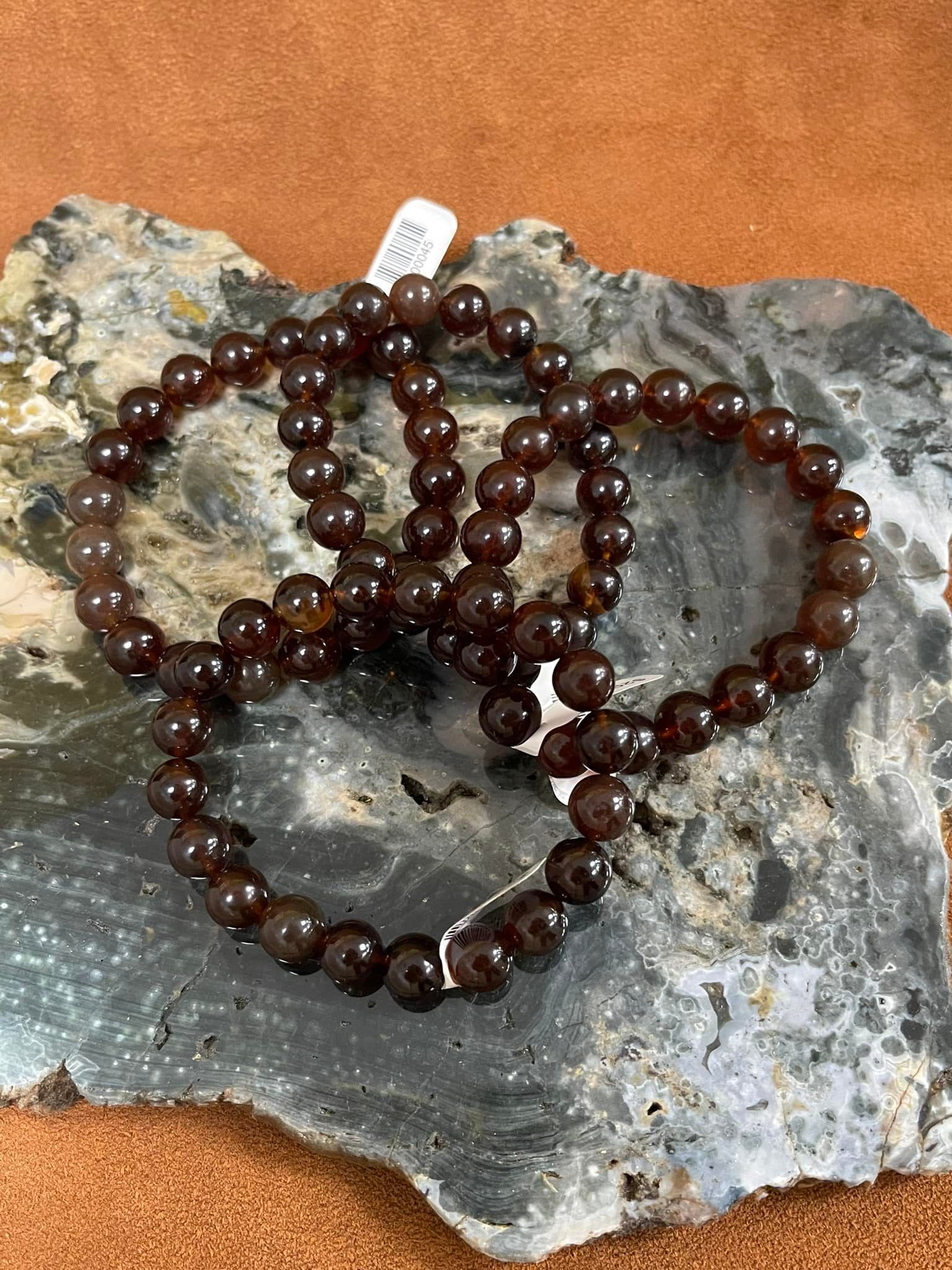 Three brown beaded bracelets rest on a dark gray and white rock in a USA shop.