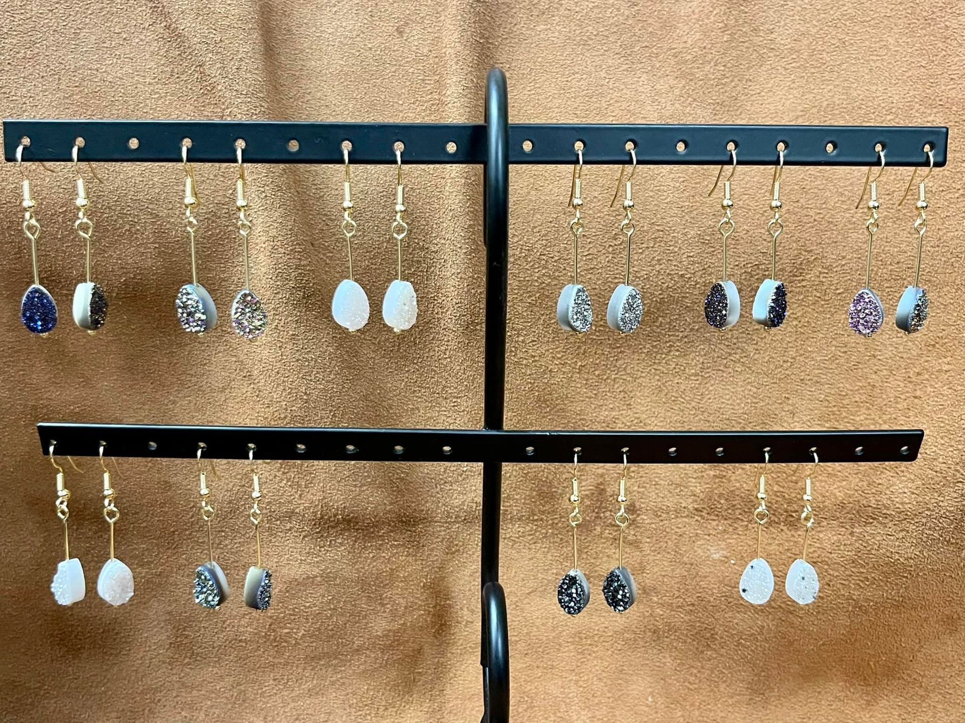 Earrings displayed on a black metal stand, showcasing various gemstone colors.