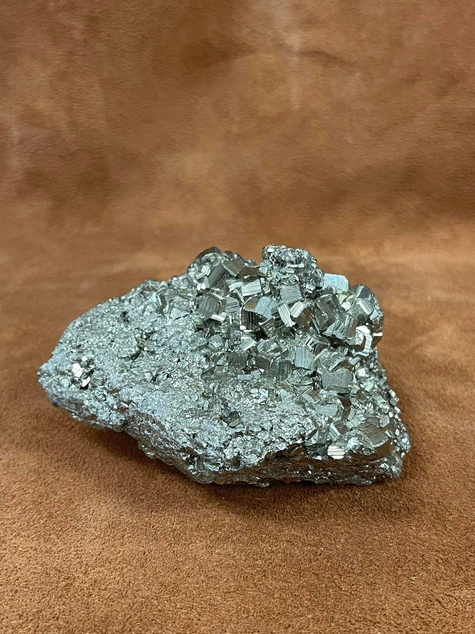 Pyrite crystal cluster, metallic silver with cubic formations, on brown backdrop.