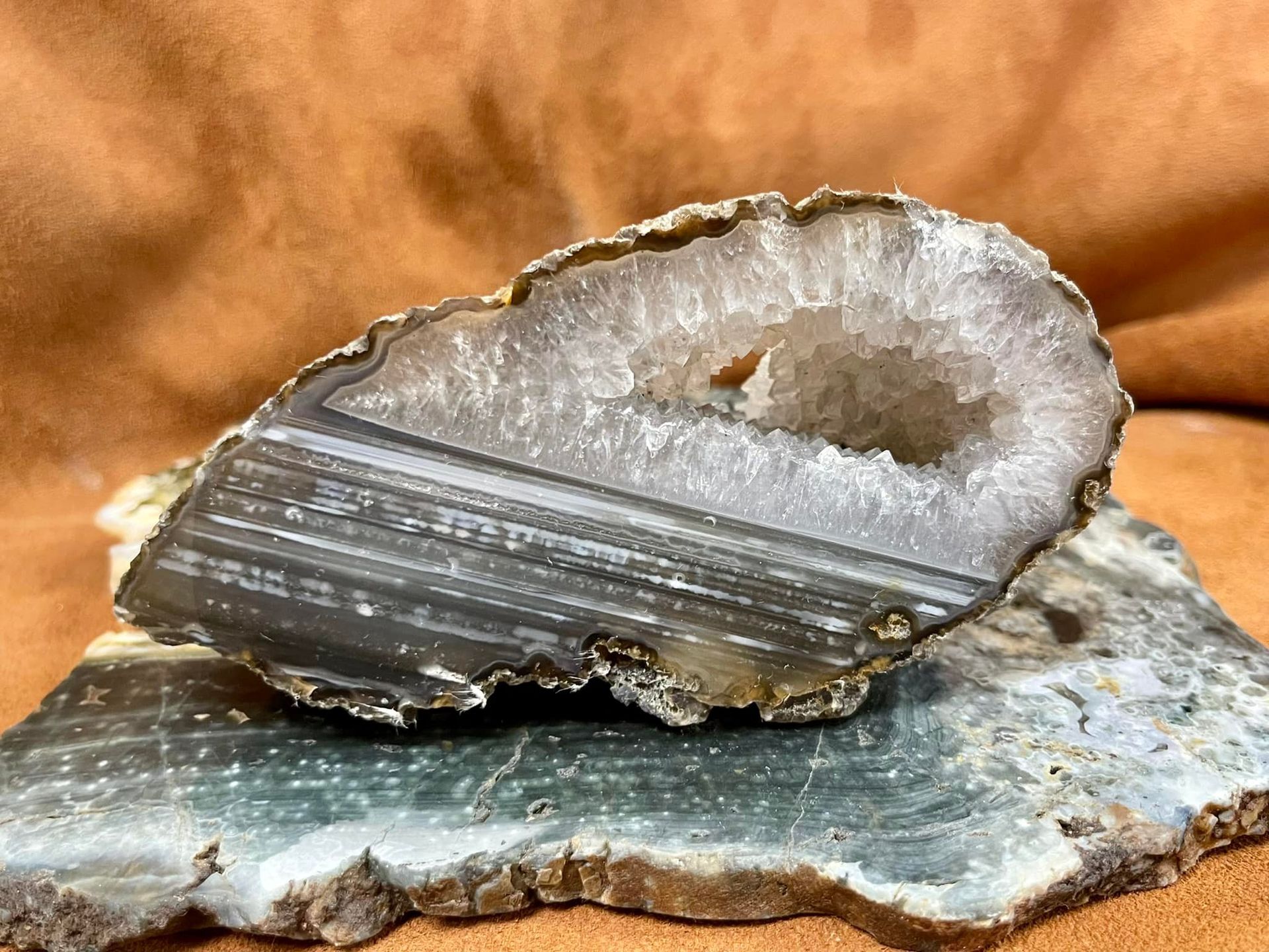 Agate geode, cut open to reveal a crystal-lined cavity, resting on a flat, blue-green stone slab.
