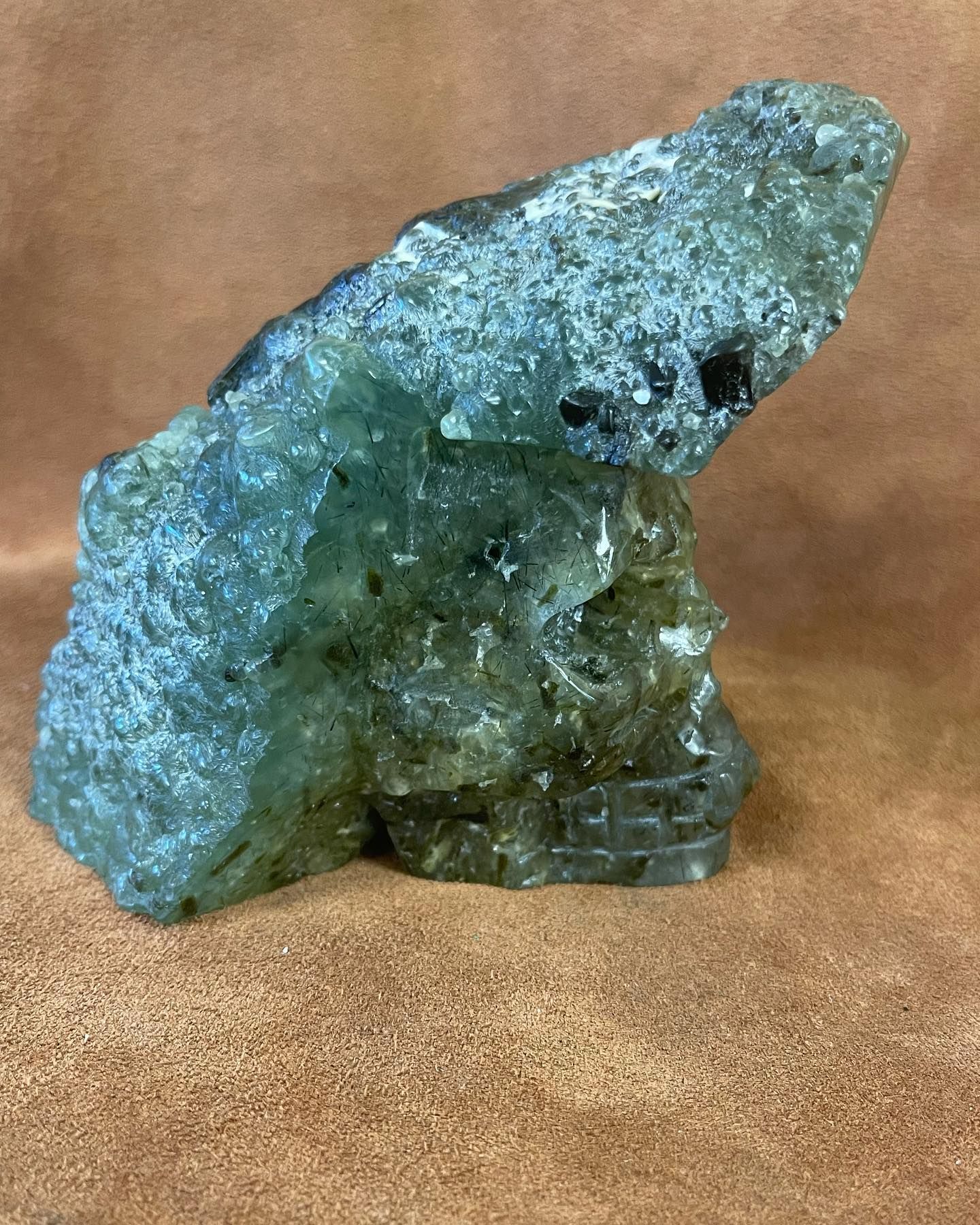 Green, rough-hewn stone carving of a stylized skull, set against a brown background.