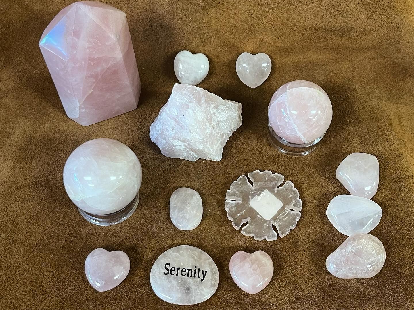 Rose quartz crystals of various shapes on a brown surface, including spheres, hearts, and a large faceted piece.