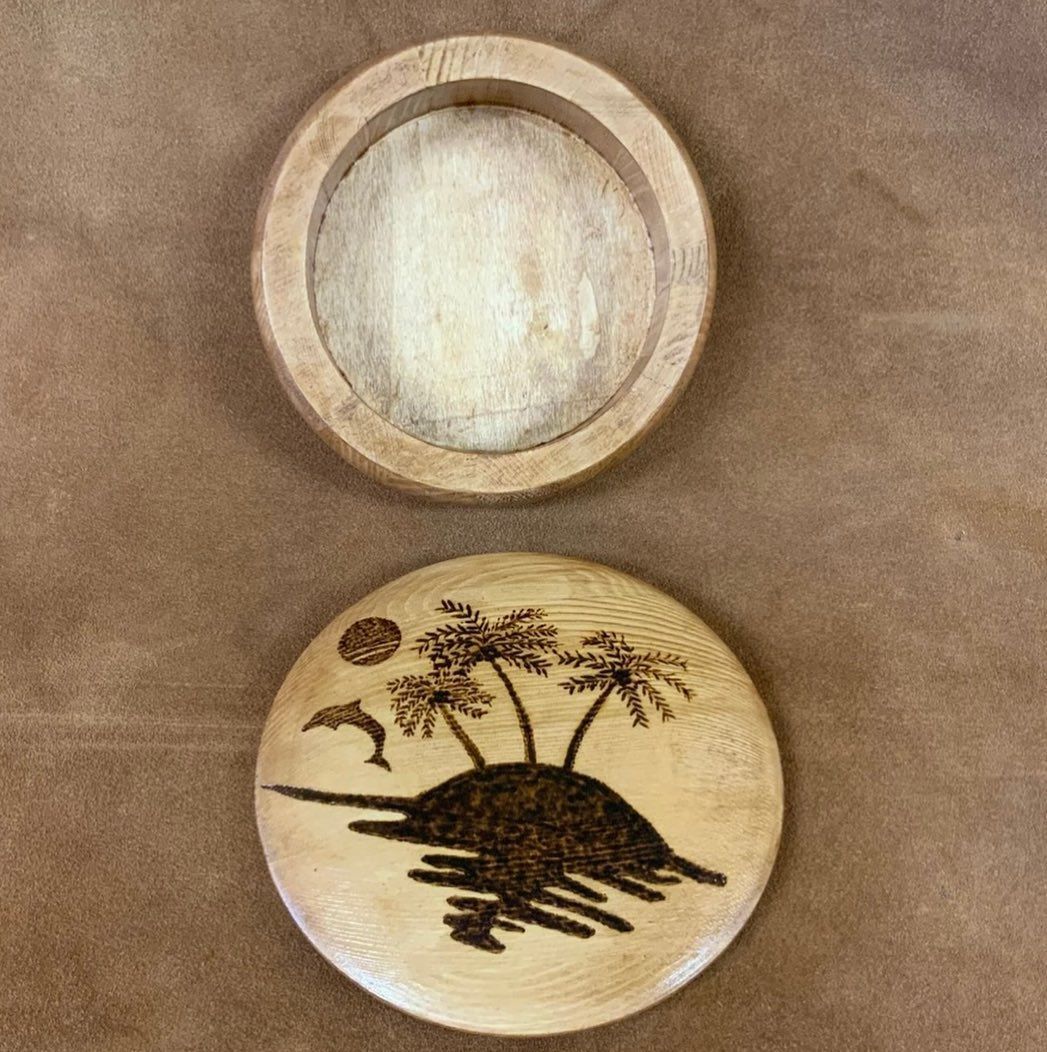 Wooden box, top open, with island scene etched on lid and light-colored interior. Brown backdrop.