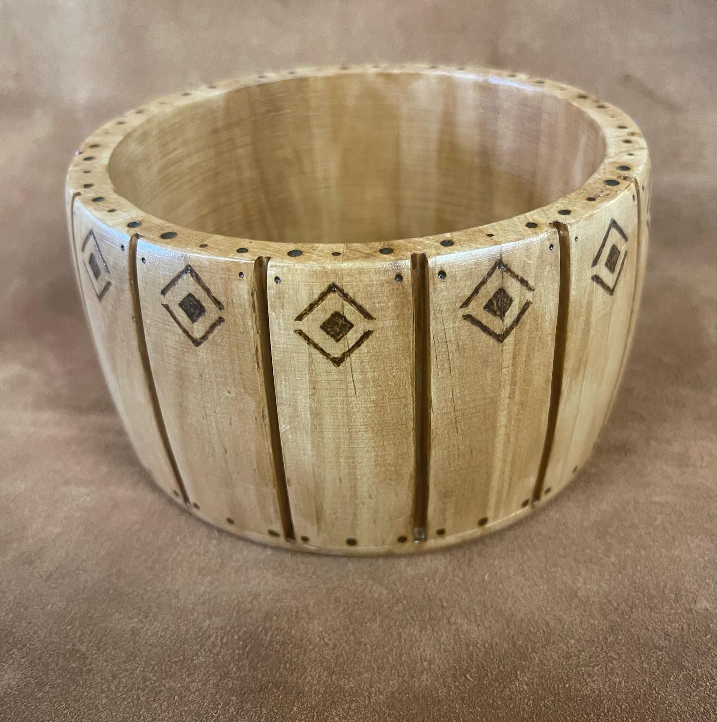 Wooden bowl with dark vertical lines and diamond patterns on the outside.