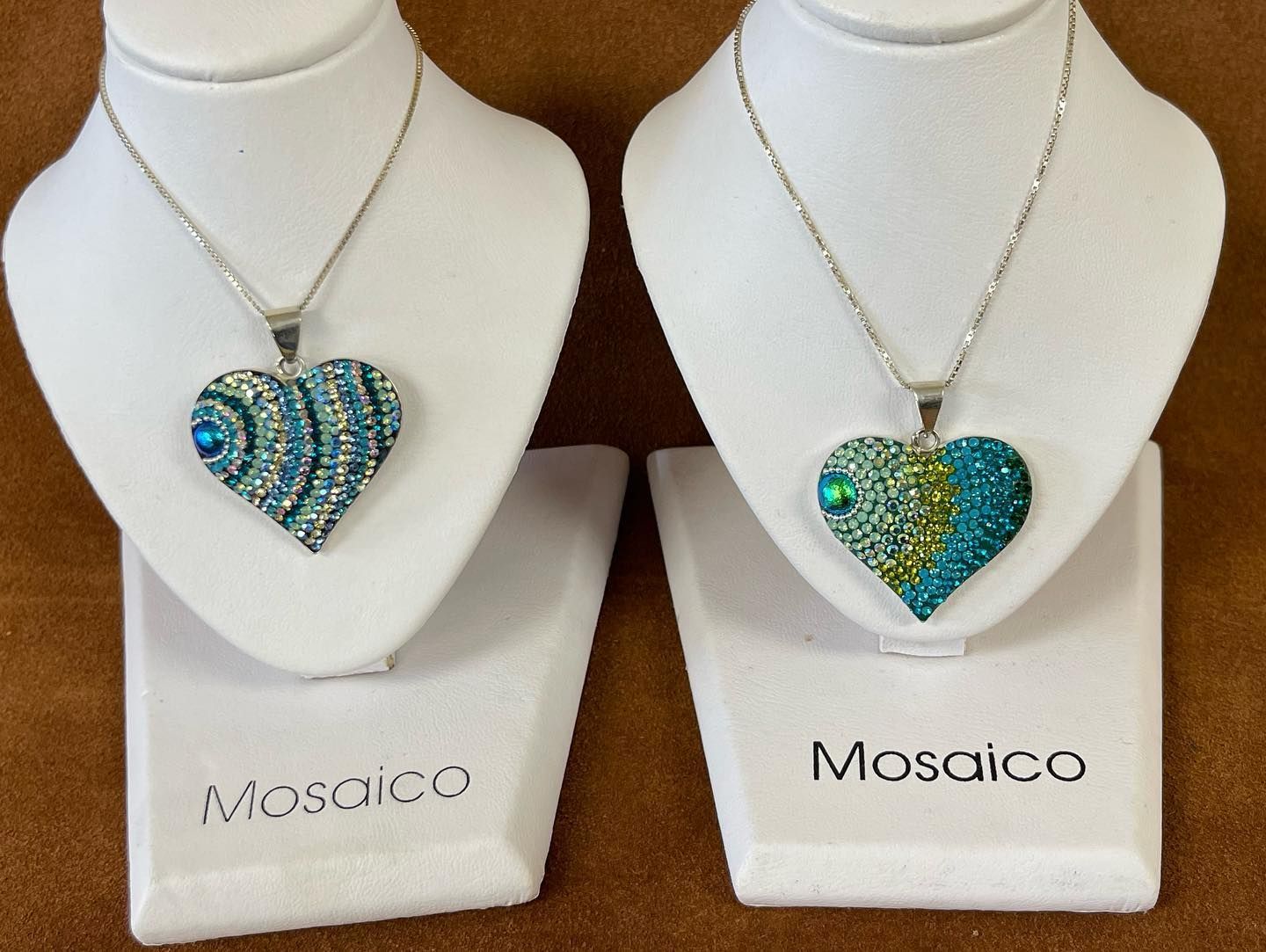 Two heart-shaped jeweled pendants displayed on white stands with 