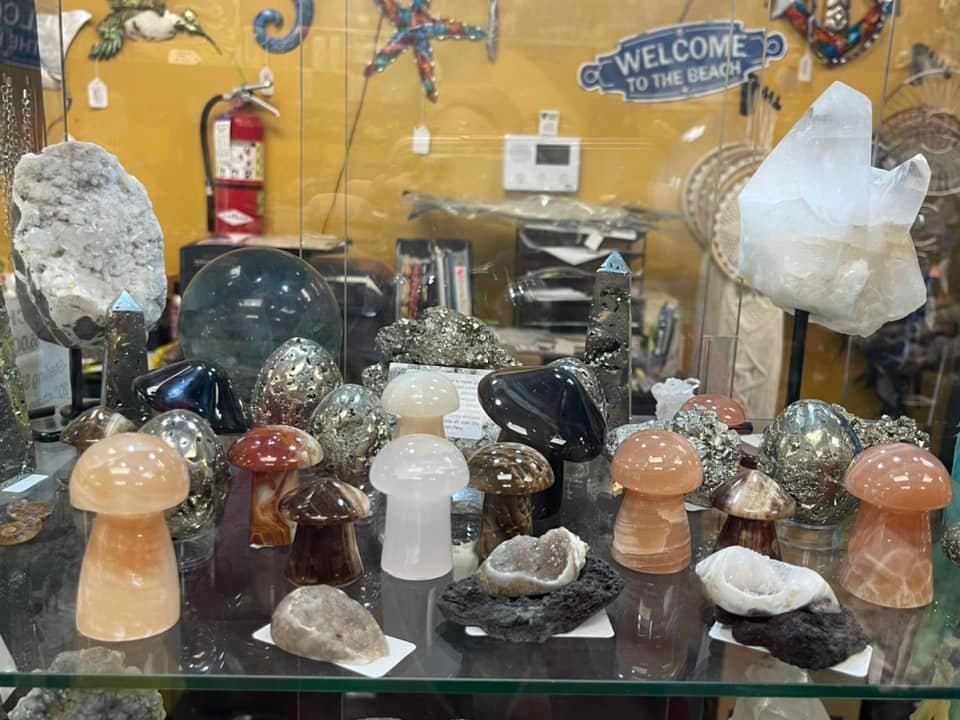 A shop display featuring crystal mushrooms, geodes, spheres, and other minerals behind a glass case.