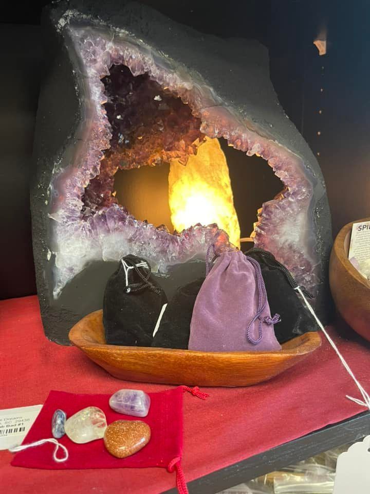 A large amethyst geode with a light inside, display with crystals and bags.