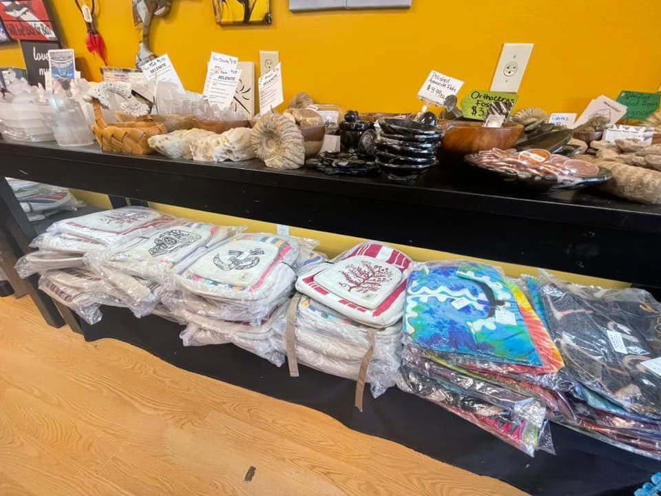 Shop display of various items: pottery, coasters, and fabric bags on a black counter. Yellow wall and wood floor.