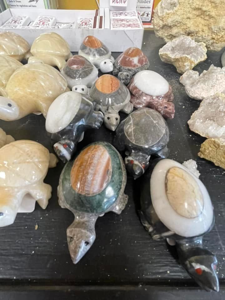 Various carved stone turtle figurines displayed on a dark surface, alongside some rock formations.