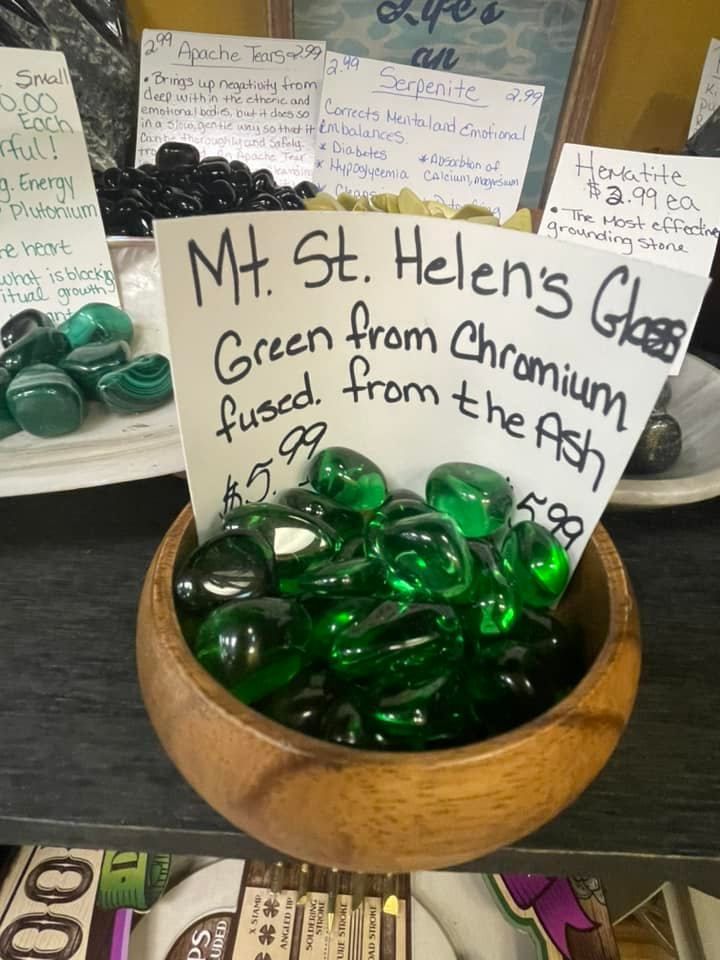 A wooden bowl filled with green, shiny glass stones labeled 
