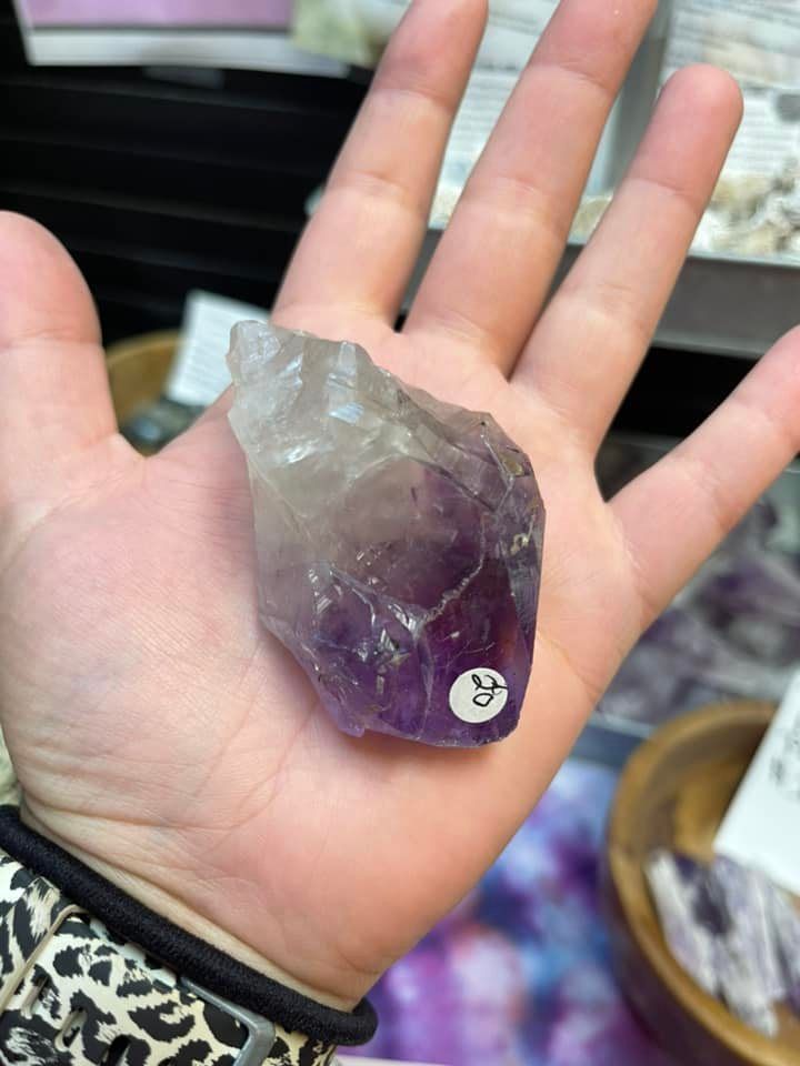 Hand holding a raw, purple amethyst crystal with a price tag in a shop.