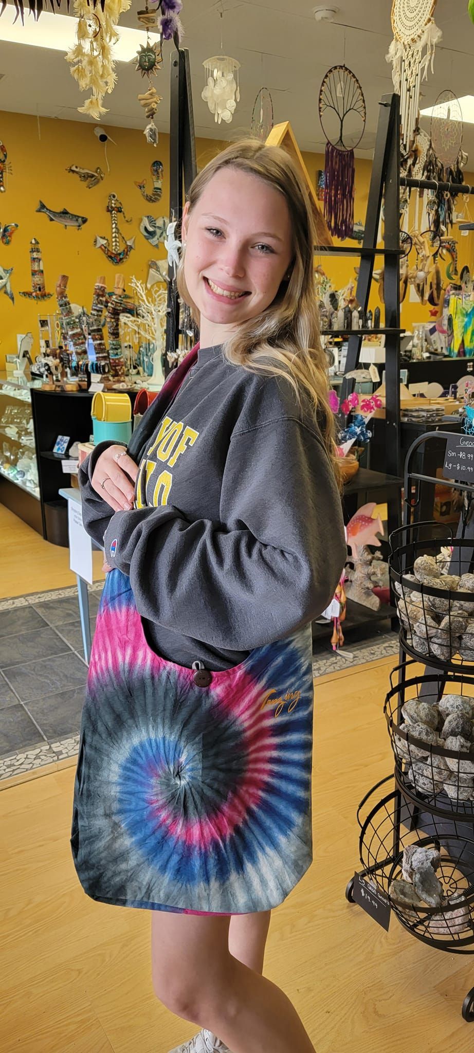 A smiling person holding a tie-dye bag inside a shop with trinkets.