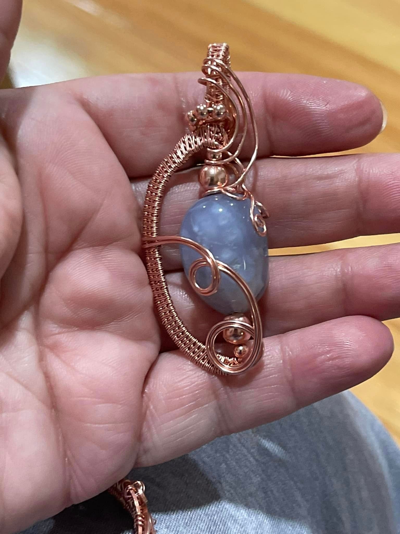 Hand holding a copper wire-wrapped pendant with a blue stone in a USA shop.
