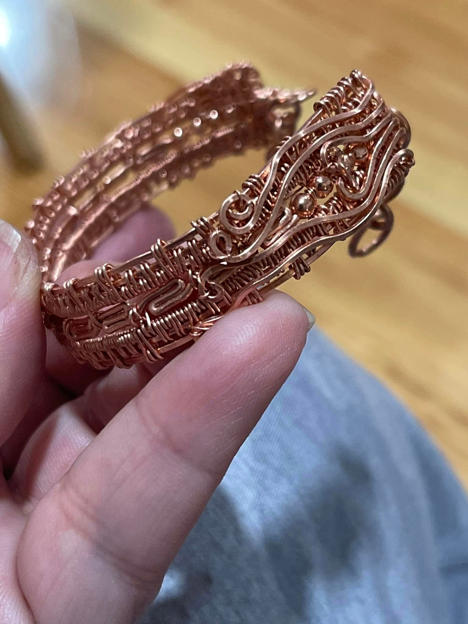 Copper wire-wrapped bracelet held in hand, intricate woven design in a USA shop.