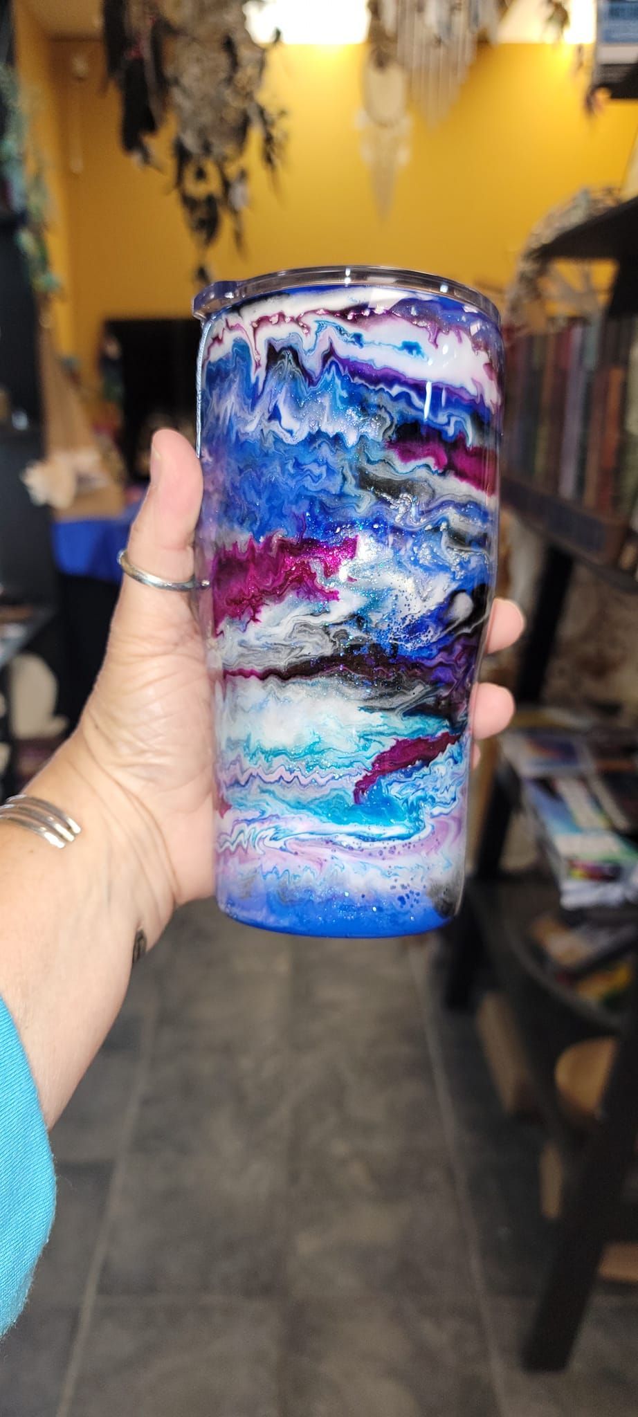 Hand holding a colorful tumbler with blue, purple, and white abstract design in a USA shop.