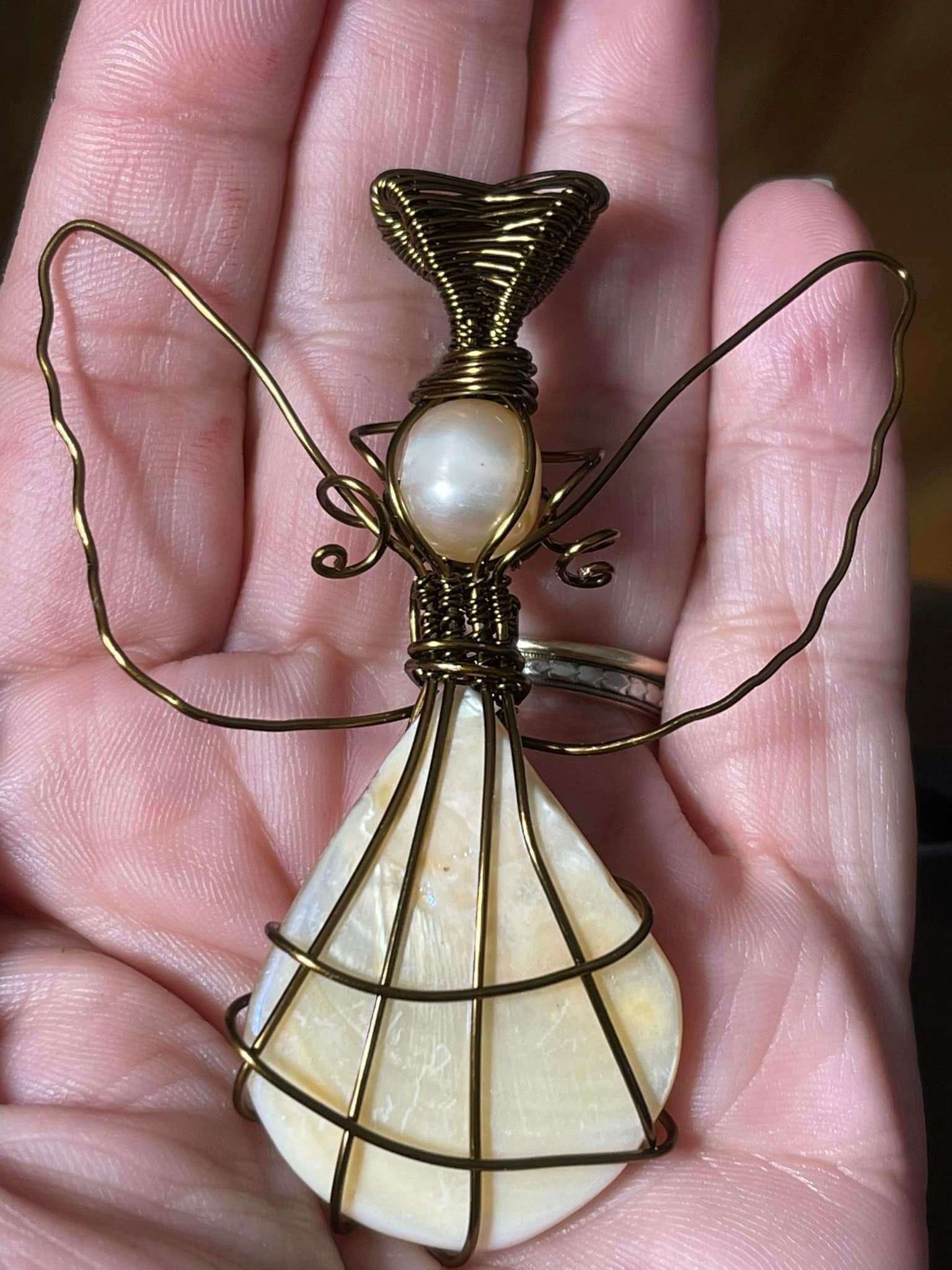 Wire-wrapped angel pendant with pearl head and shell body, held in a hand in a USA shop.