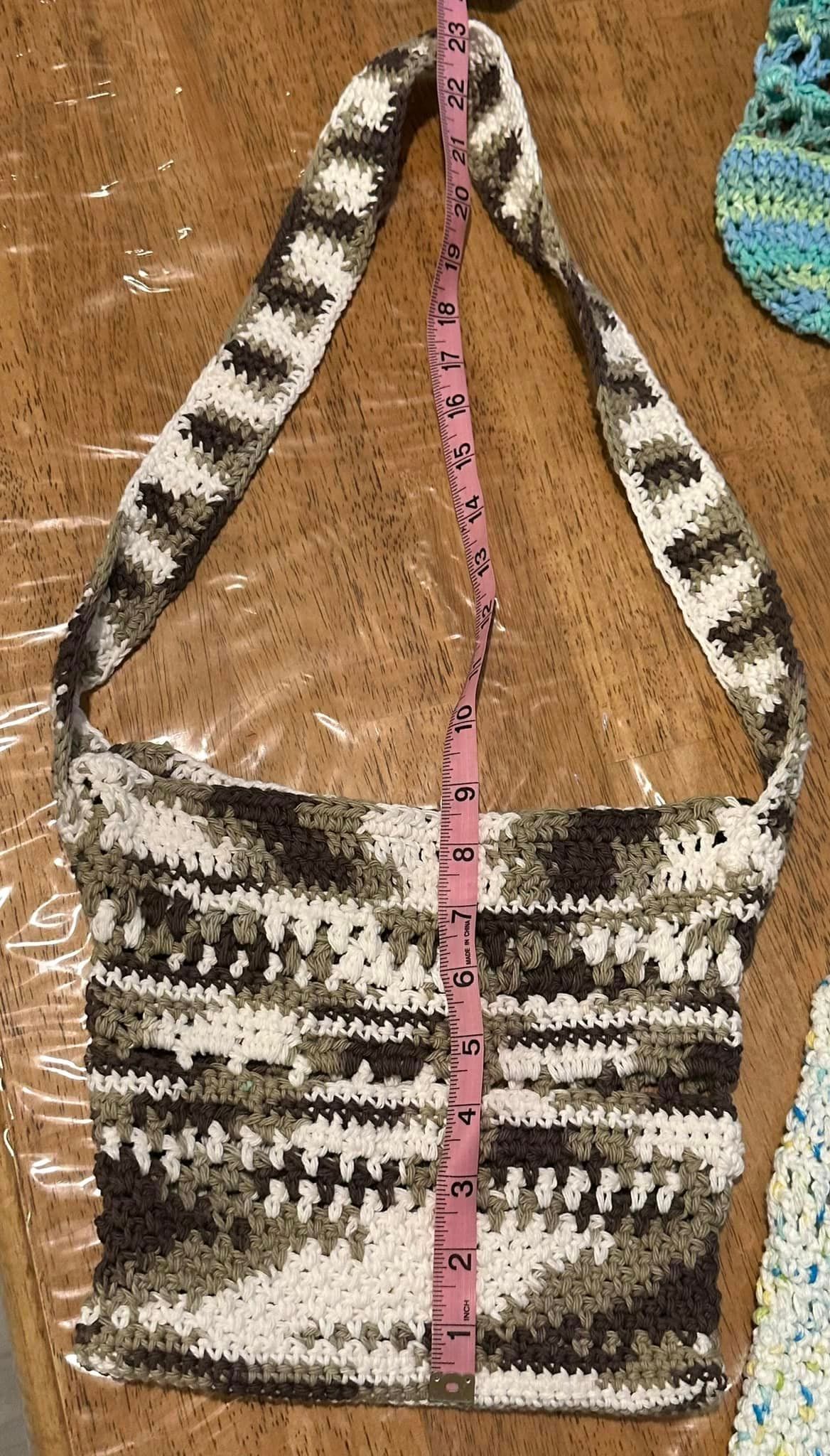Crocheted bag with strap in white, brown, and gray, being measured with a pink ruler.