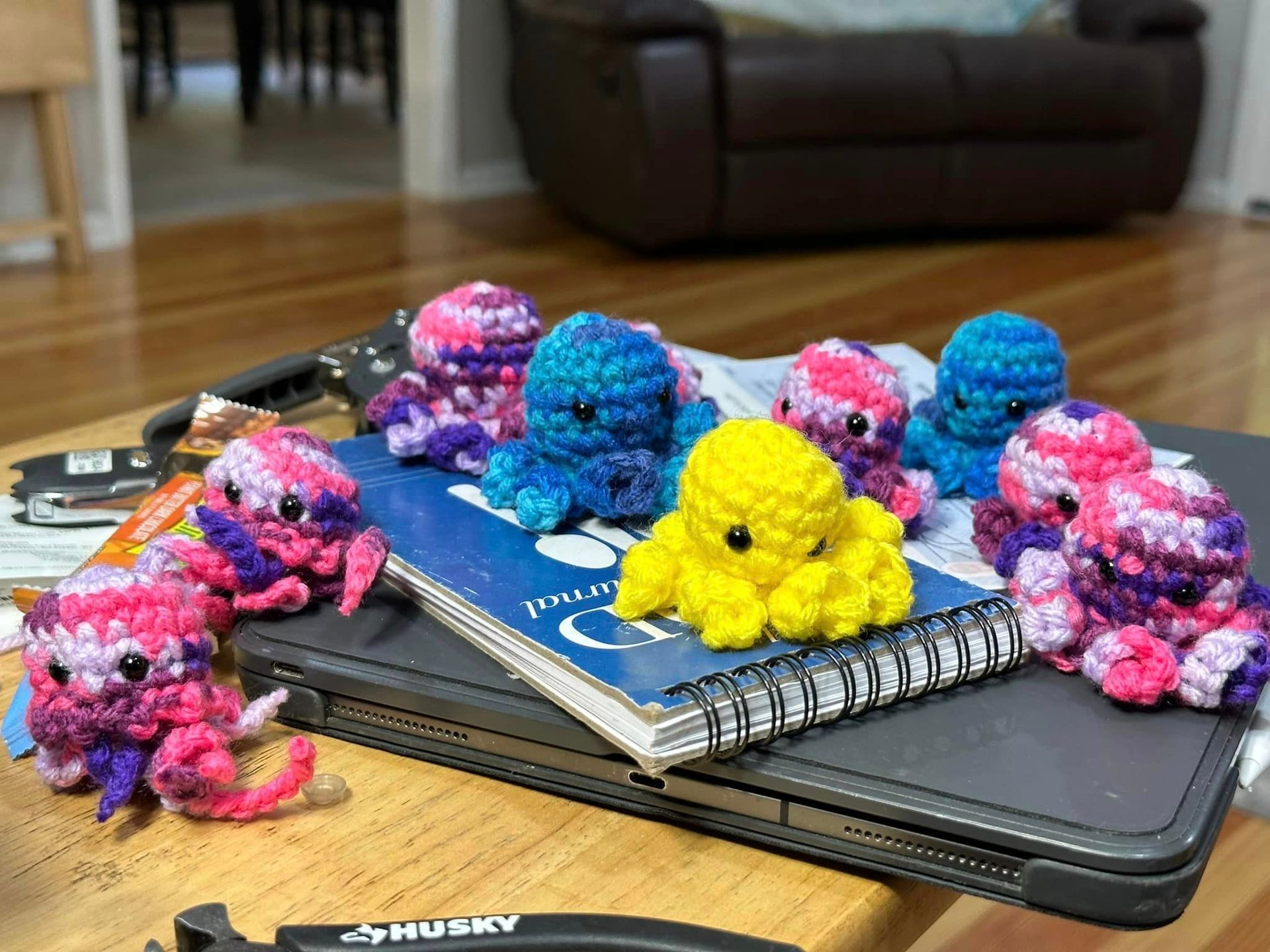 Crocheted colorful octopus toys on a laptop and journal, on a table in a home.