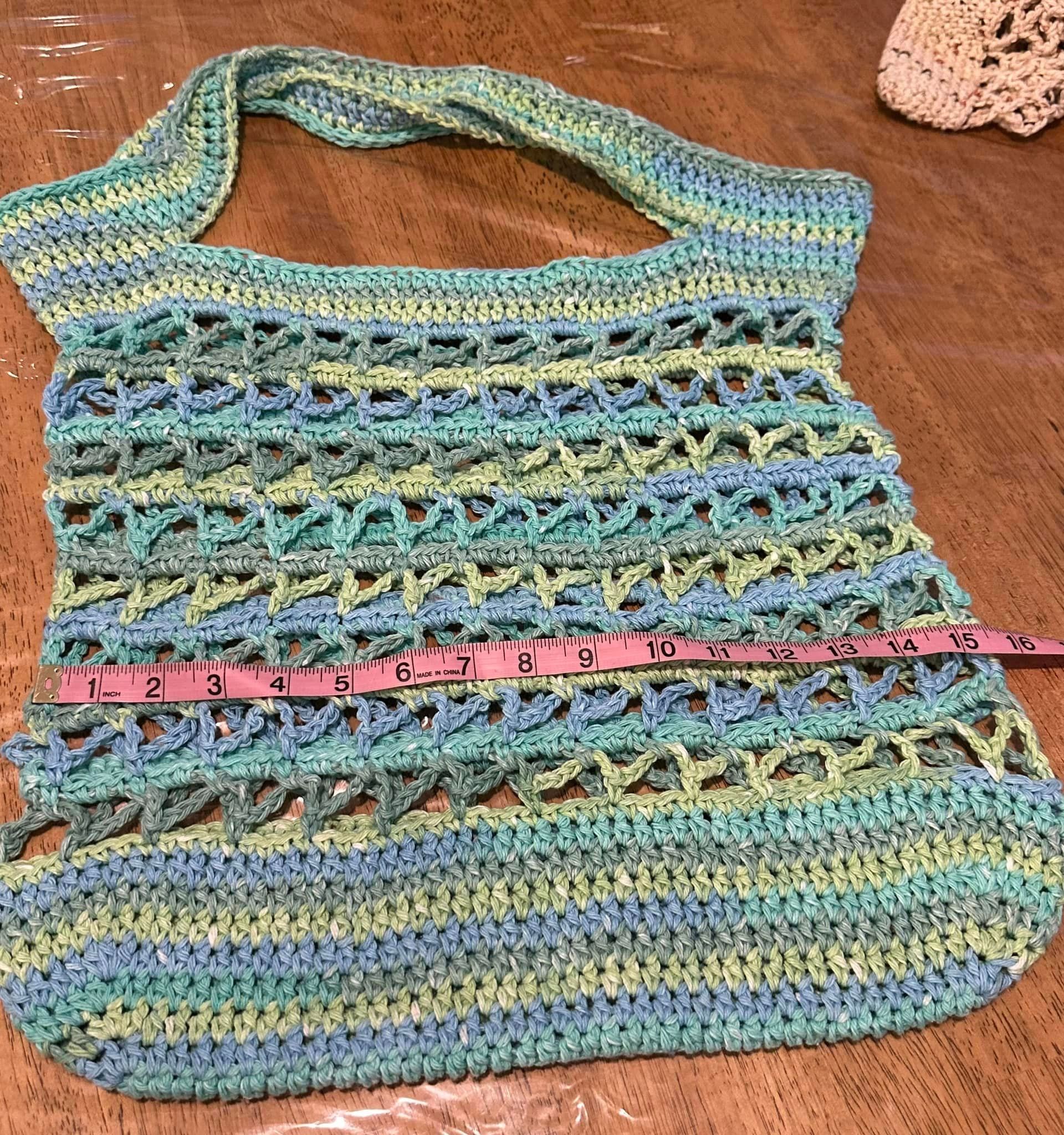 Crocheted tote bag, blue and green yarn with openwork design, laid on a table; ruler shows width.