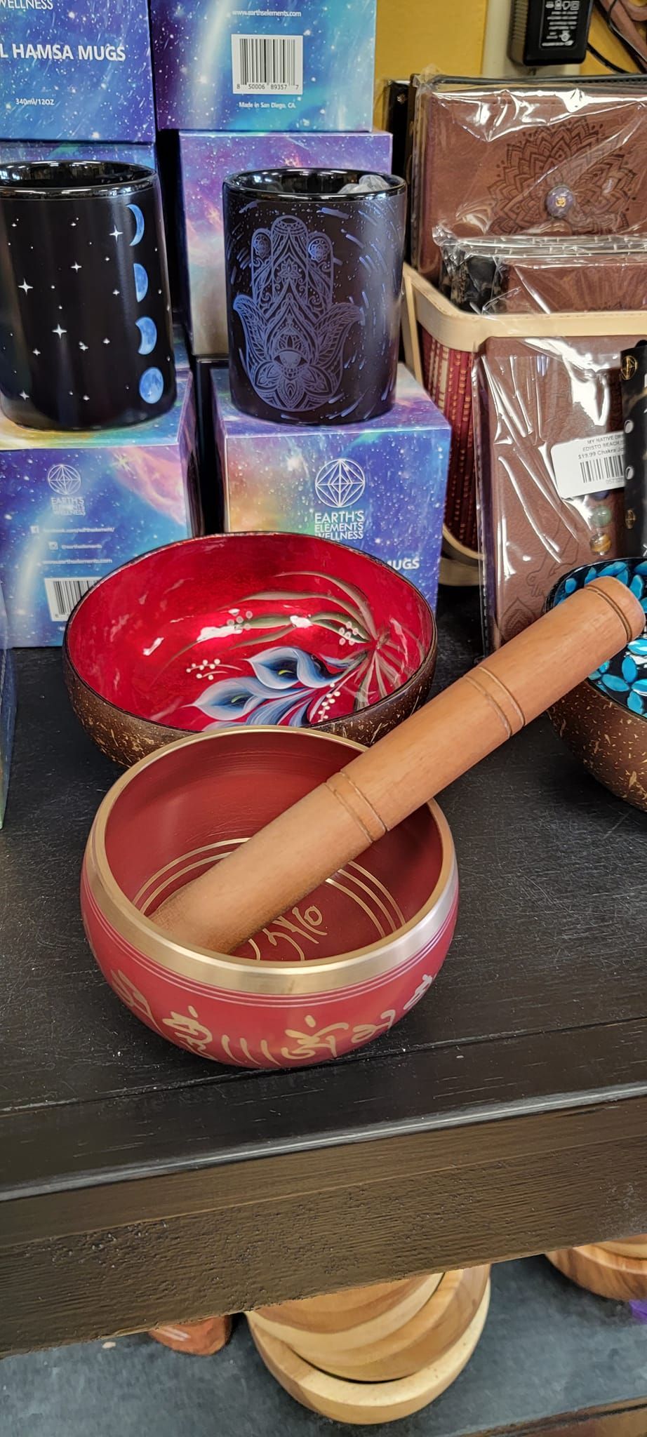 A red and gold singing bowl with a mallet inside, with other items on a shelf.