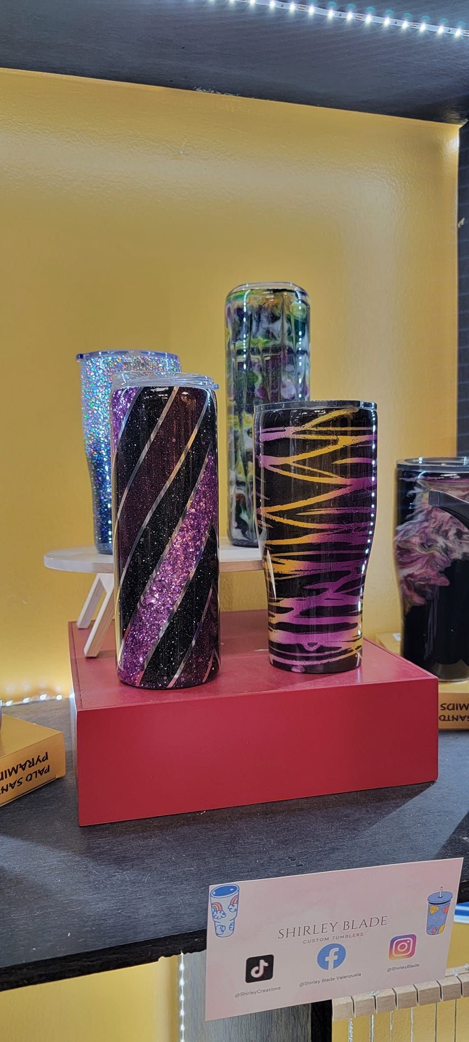 Colorful, patterned cylindrical objects displayed on a red platform. Yellow background, under white lights.
