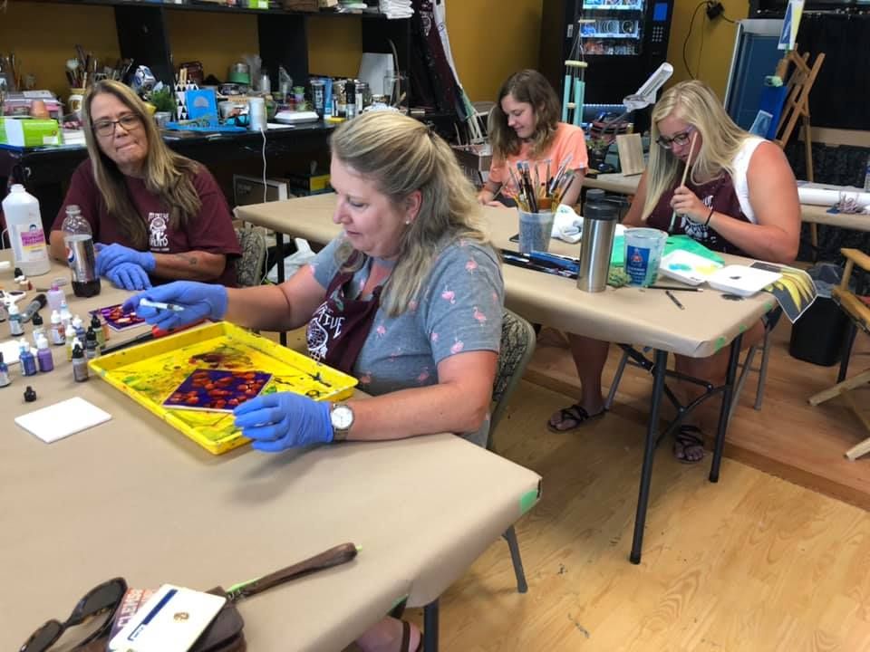 Four women at tables in an art class, marbling paper with colors.