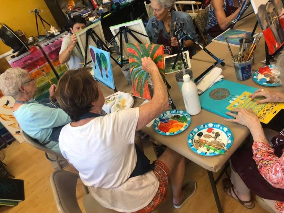 A group of women in a painting class, creating art with brushes and paint.