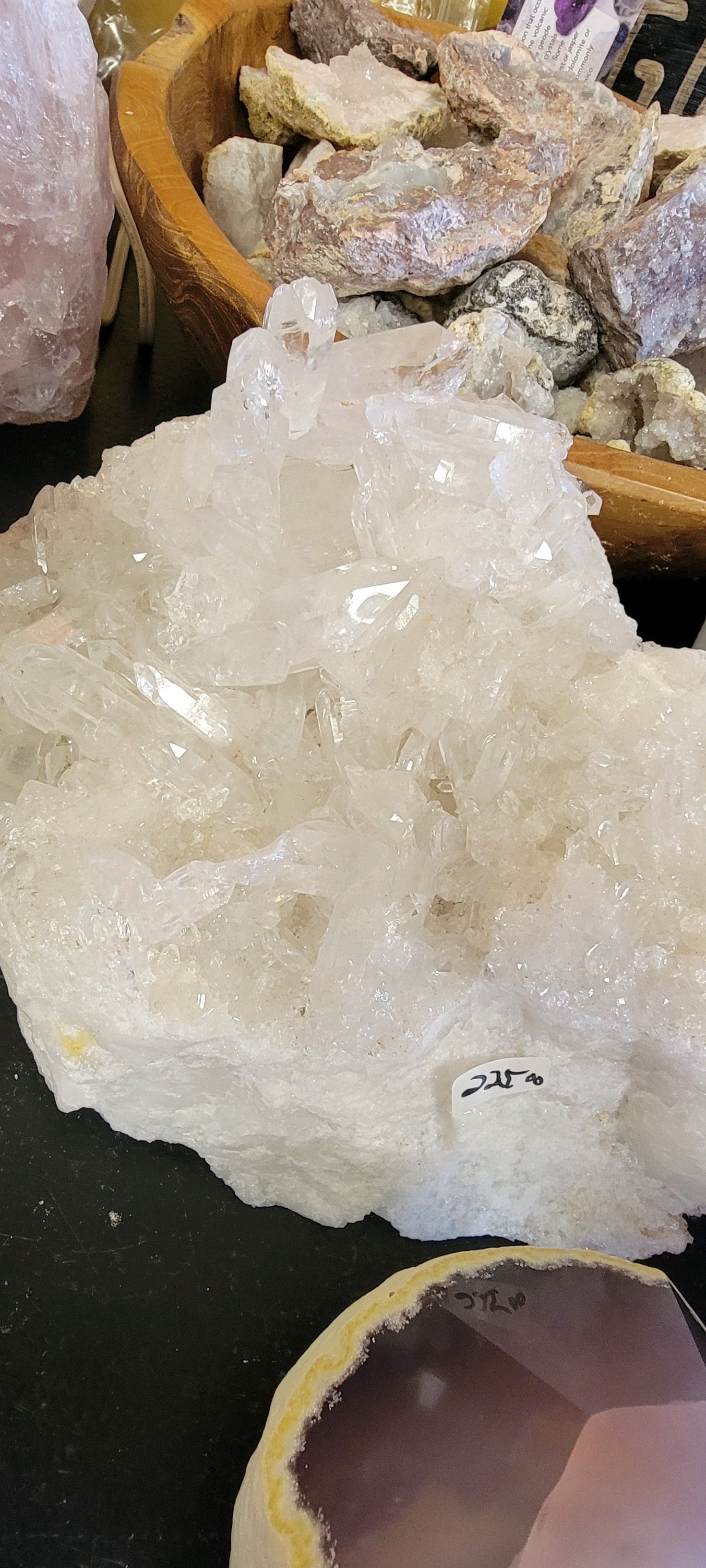 White crystal cluster with sparkles, in a shop setting with other crystals and stones.