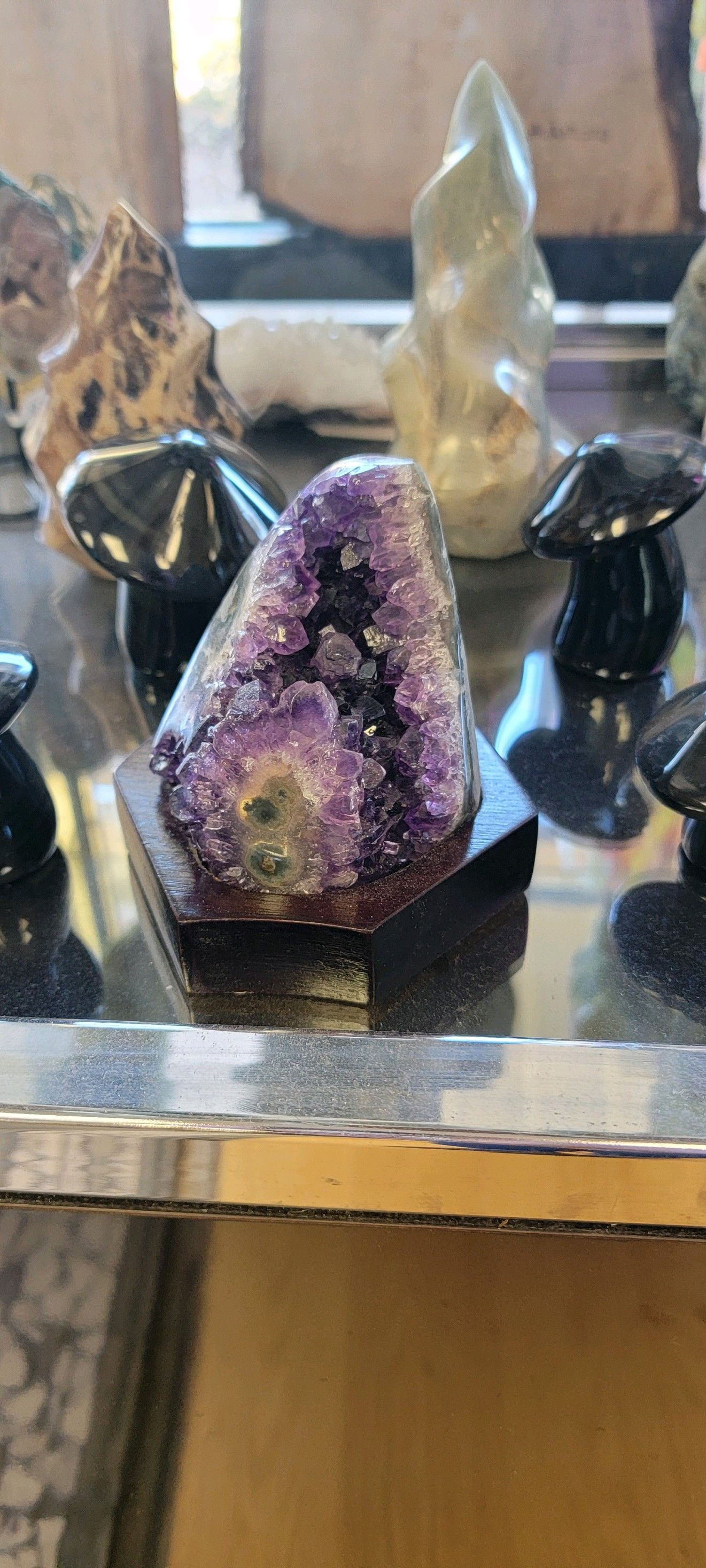 Purple amethyst geode on a black stand, displayed with other crystals and stones in a USA shop setting.