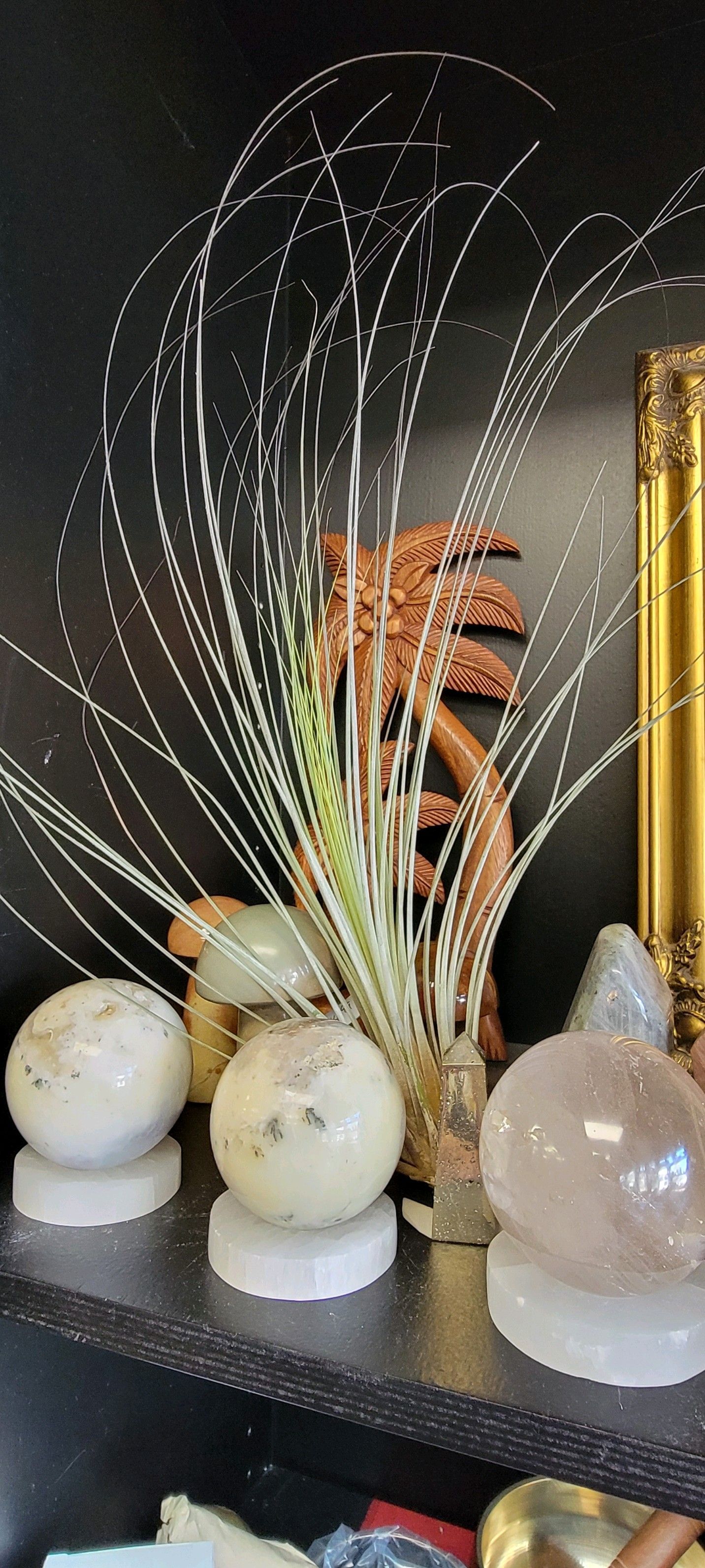 Three crystal spheres on white stands, displayed with decorative grasses and a gold-framed object in a USA shop.