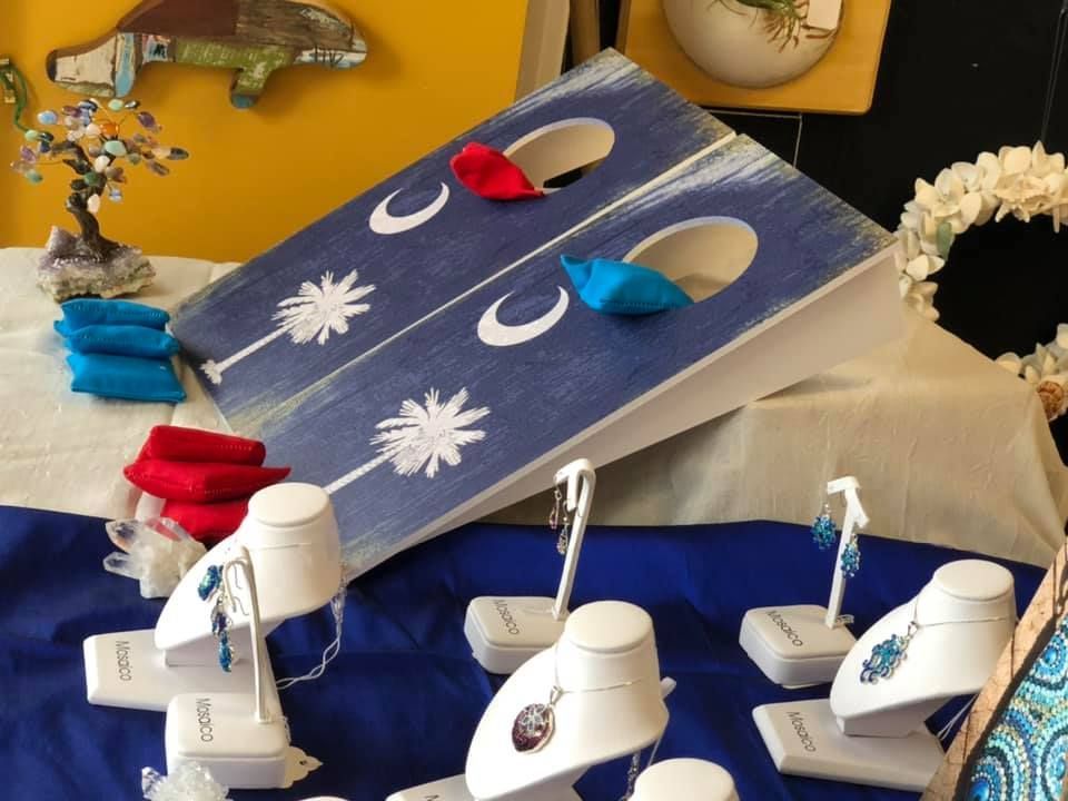Cornhole board with blue and red bean bags, jewelry display on a table.