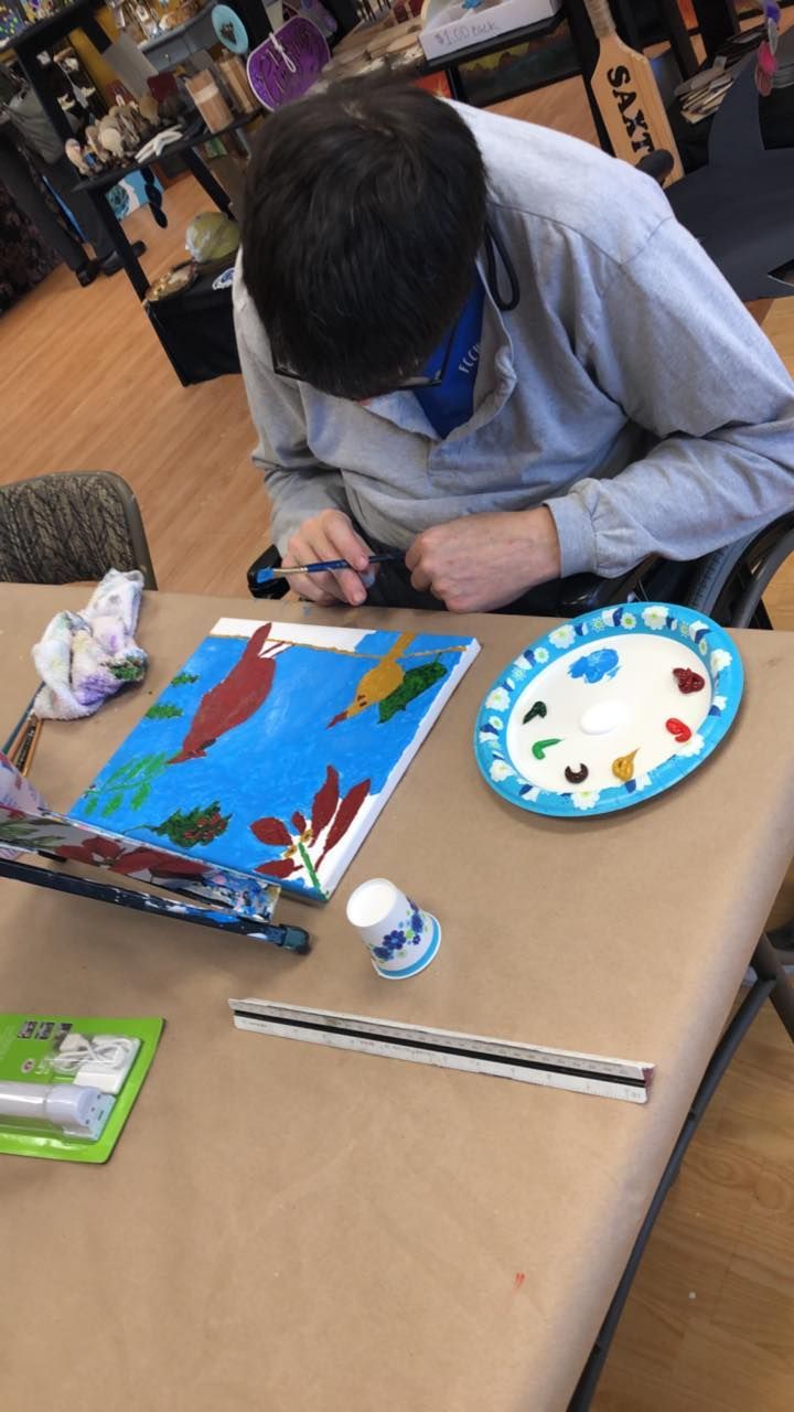 Person in wheelchair painting a seascape, using a blue, white, and red color palette.
