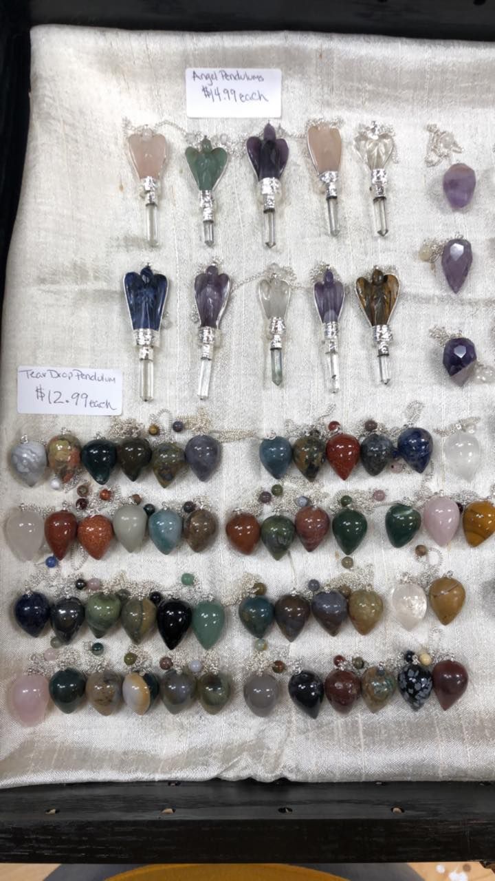 Rows of gemstone pendulums on display; white fabric background, black framed.