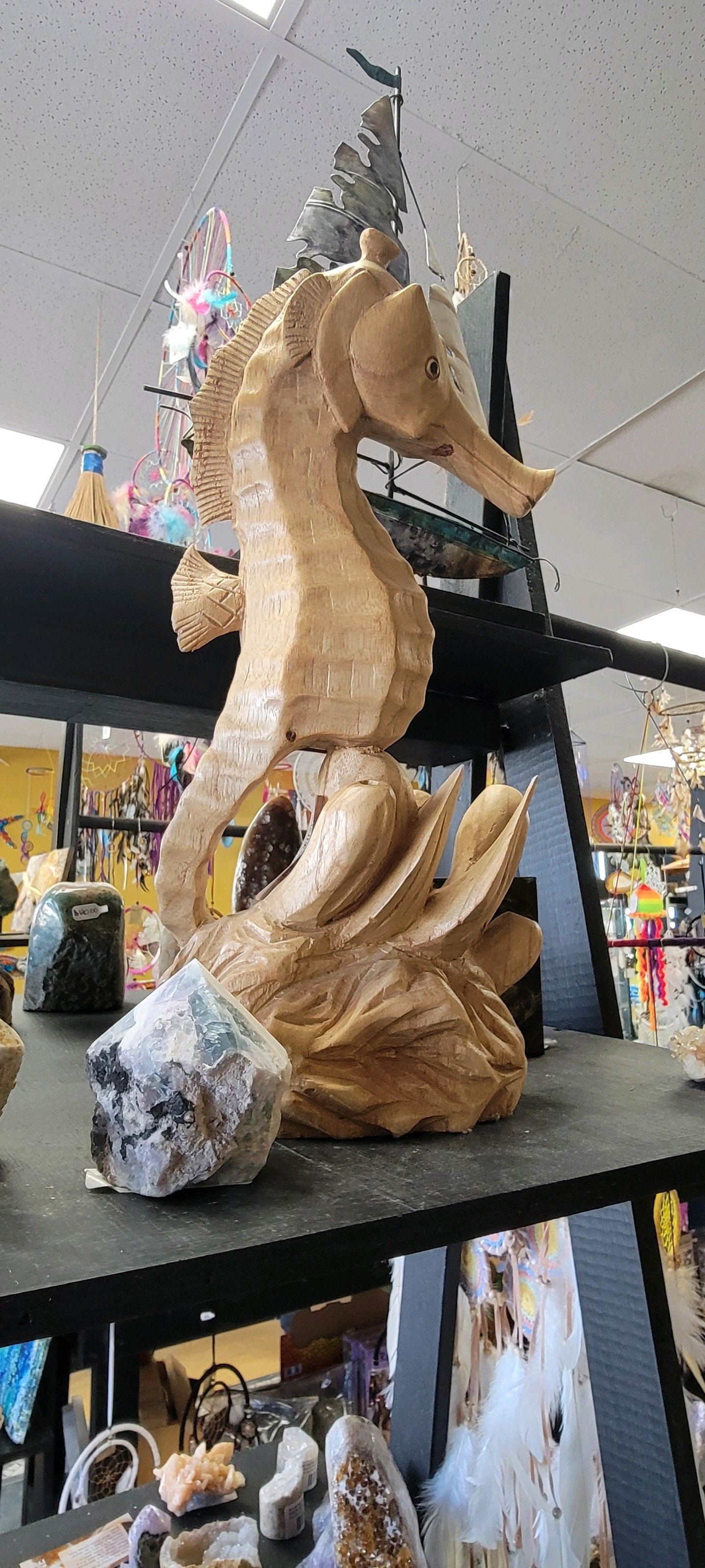 Wooden seahorse sculpture on a shelf, with a large rock at its base, displayed in a USA shop.