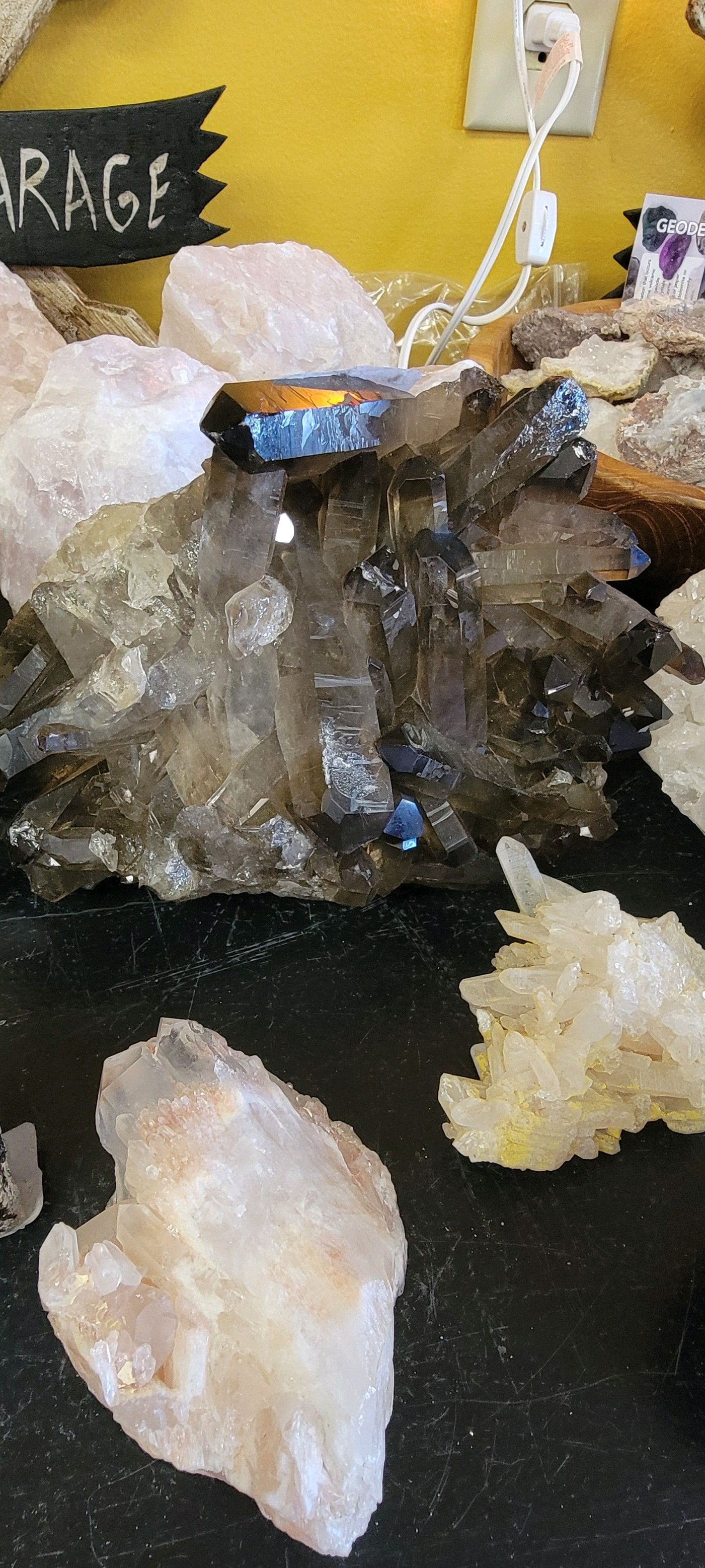 Crystals on a black surface with a yellow wall in the background. A dark cluster of crystals in the center.