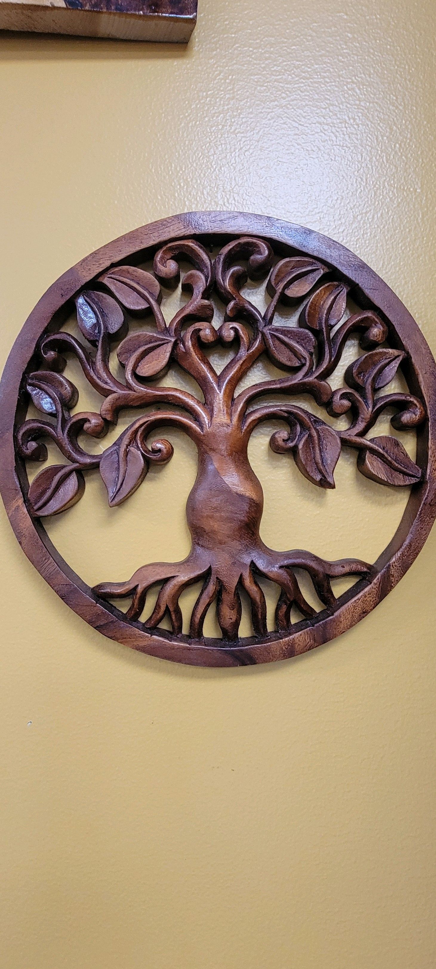 Wooden tree of life carving on a yellow wall.