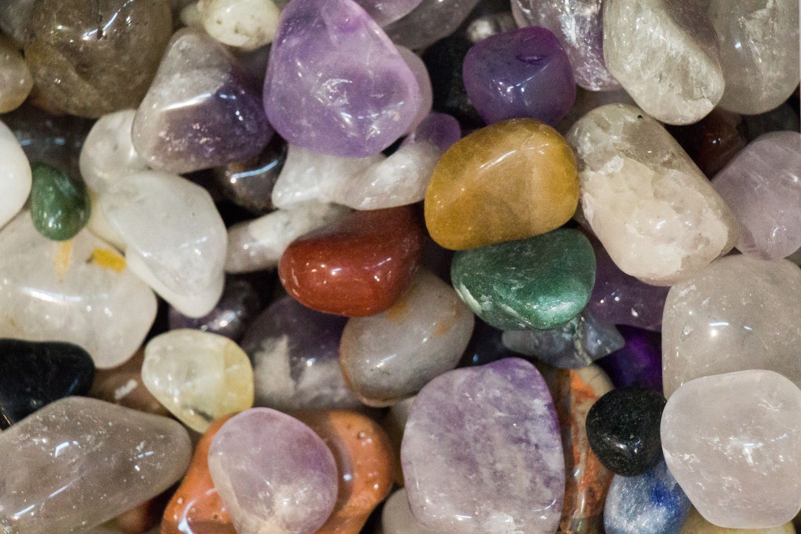 Close-up of a pile of polished gemstones in various colors including purple, red, gold, green, and white.