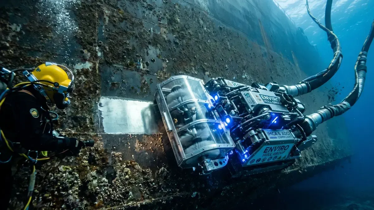 Underwater diver beside a blue-lit robotic device on a rocky seabed