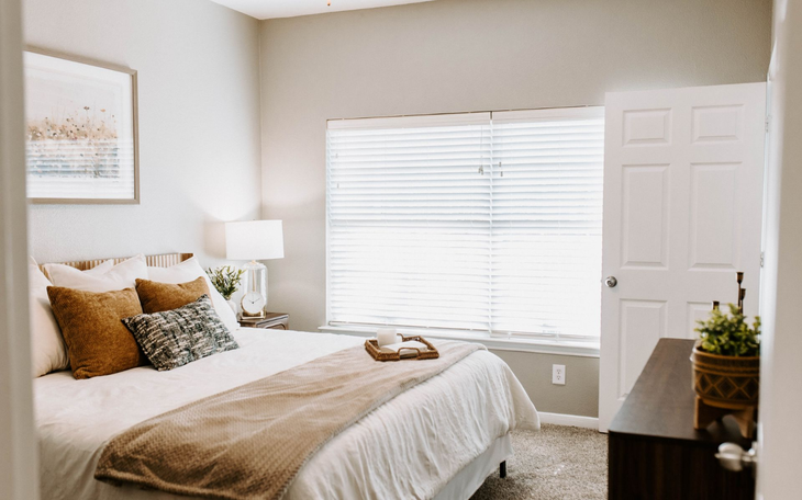 Bedroom with queen bed, desk, dark furniture, green and orange accents, ceiling fan, and window.