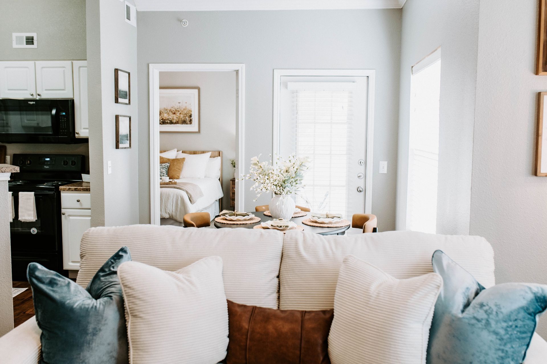 Aerial view of a residential complex with buildings, a pool, trees, and parking; lush greenery in the background.